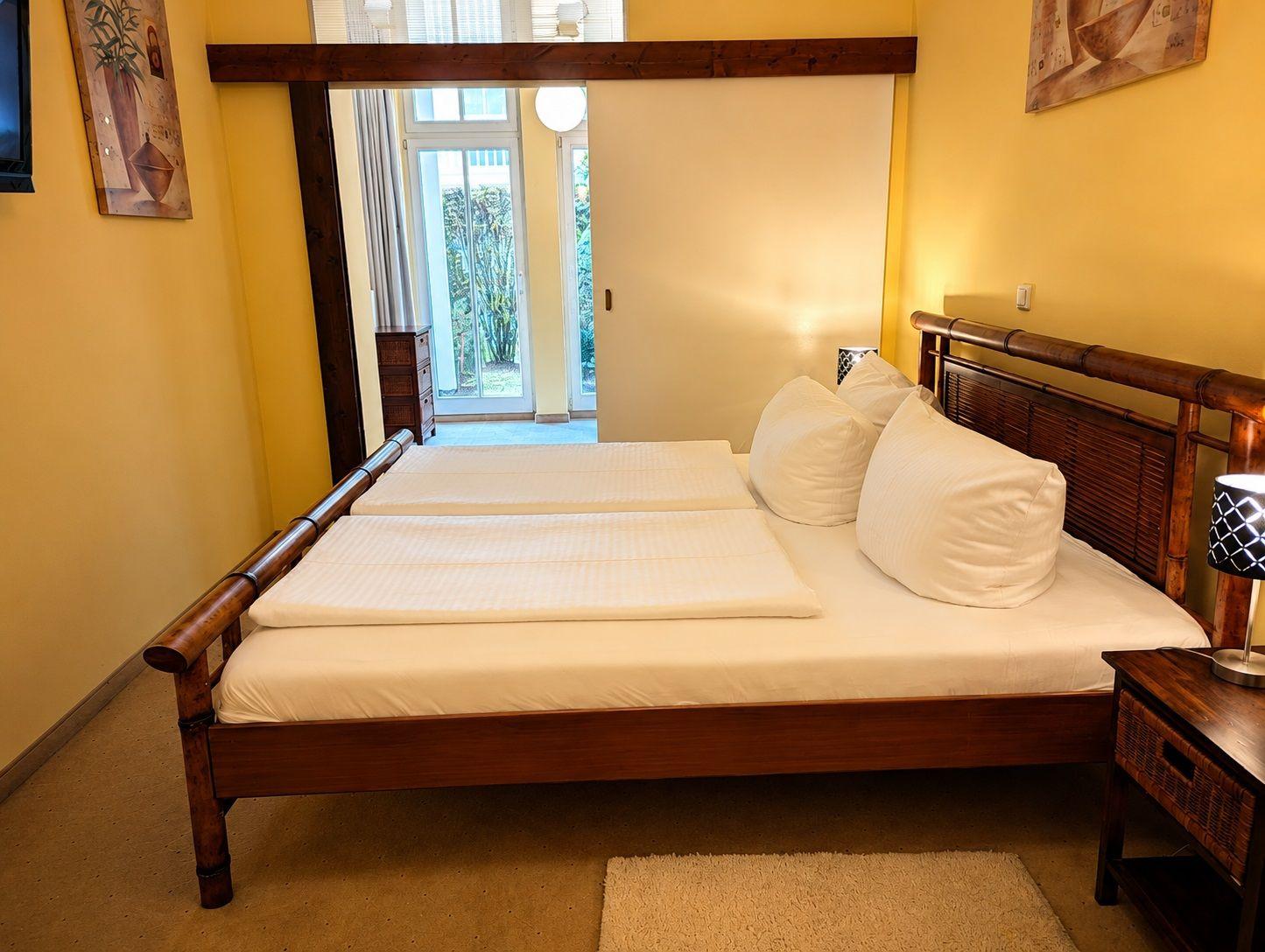 Schlafzimmer mit Holzbett, weißen Kissen und Blick auf Terrasse.