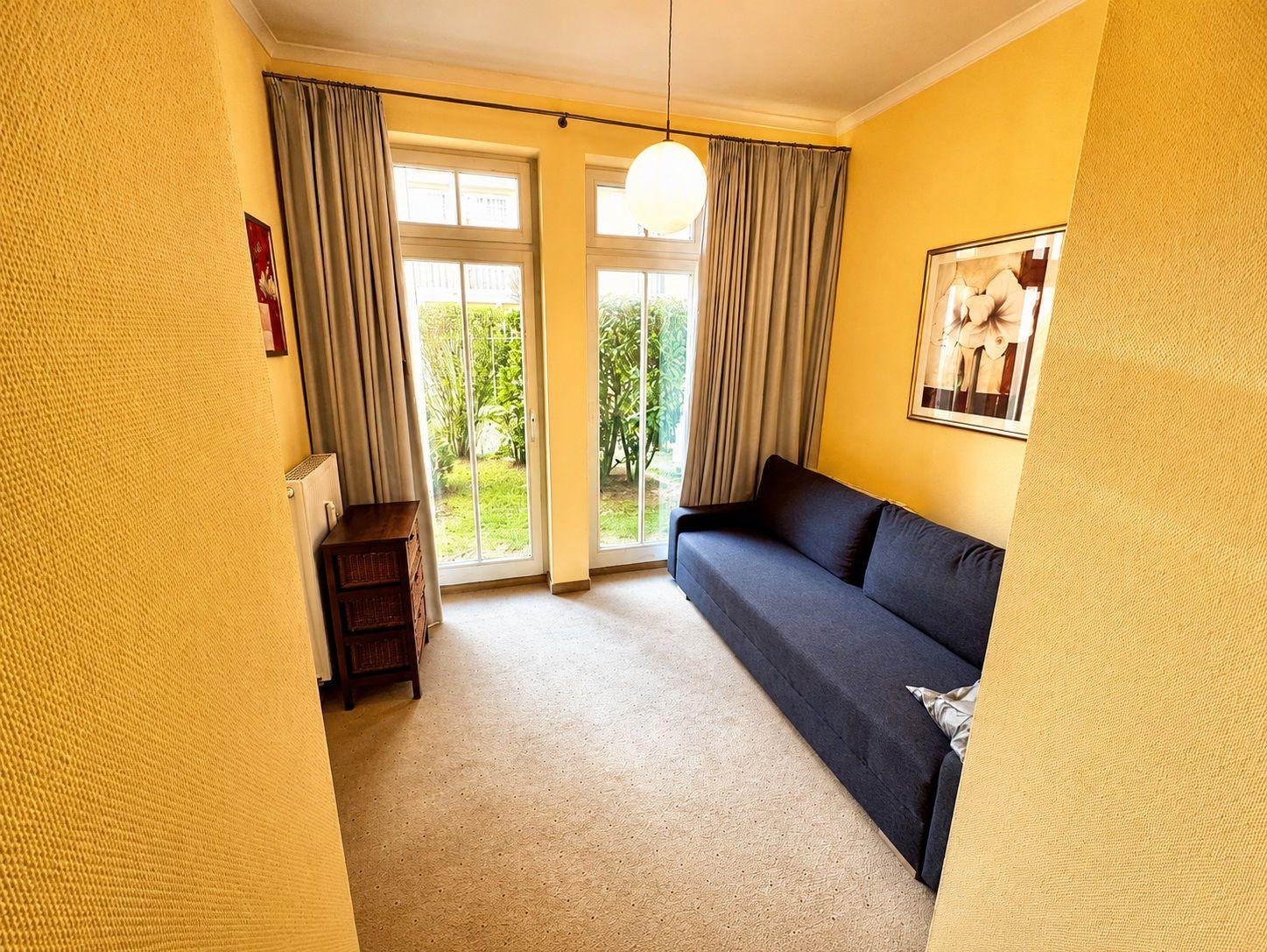 Ein Raum mit gelben Wänden, einem blauen Sofa und einer Glastür zum Garten.
