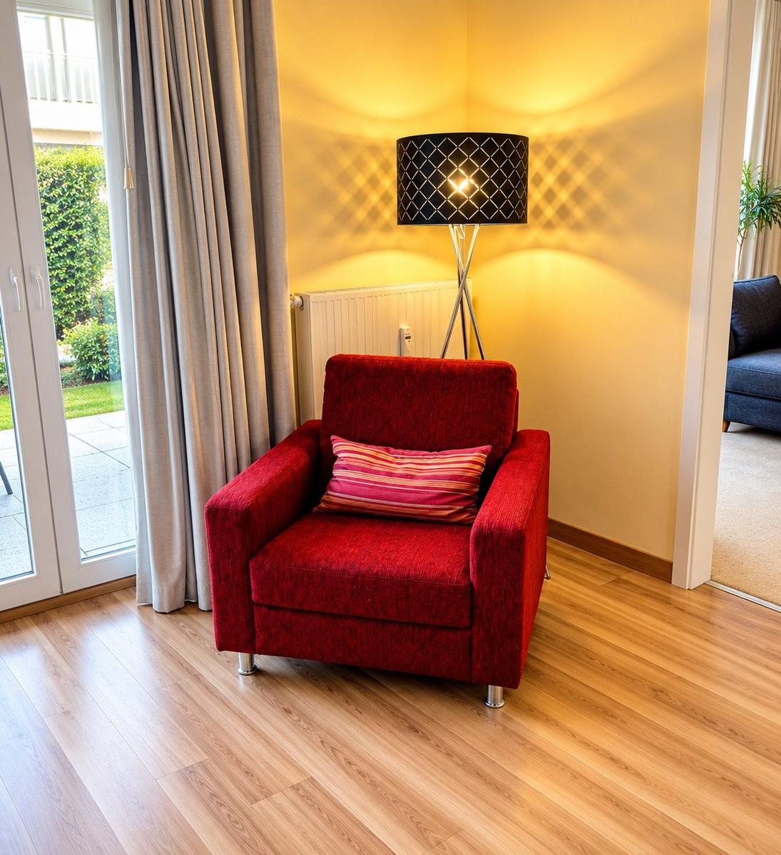 Ein roter Sessel mit Kissen steht vor einer Glastür. Eine Stehlampe und Holzboden sind sichtbar.