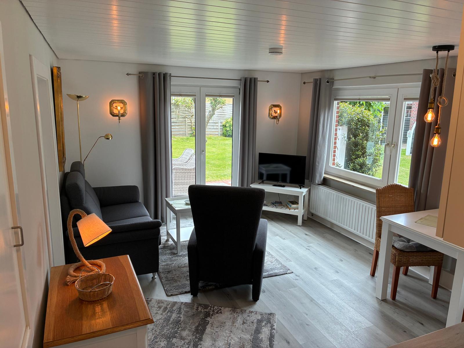 Wohnzimmer mit Sofa, Sessel, Fernseher und Blick auf Garten.