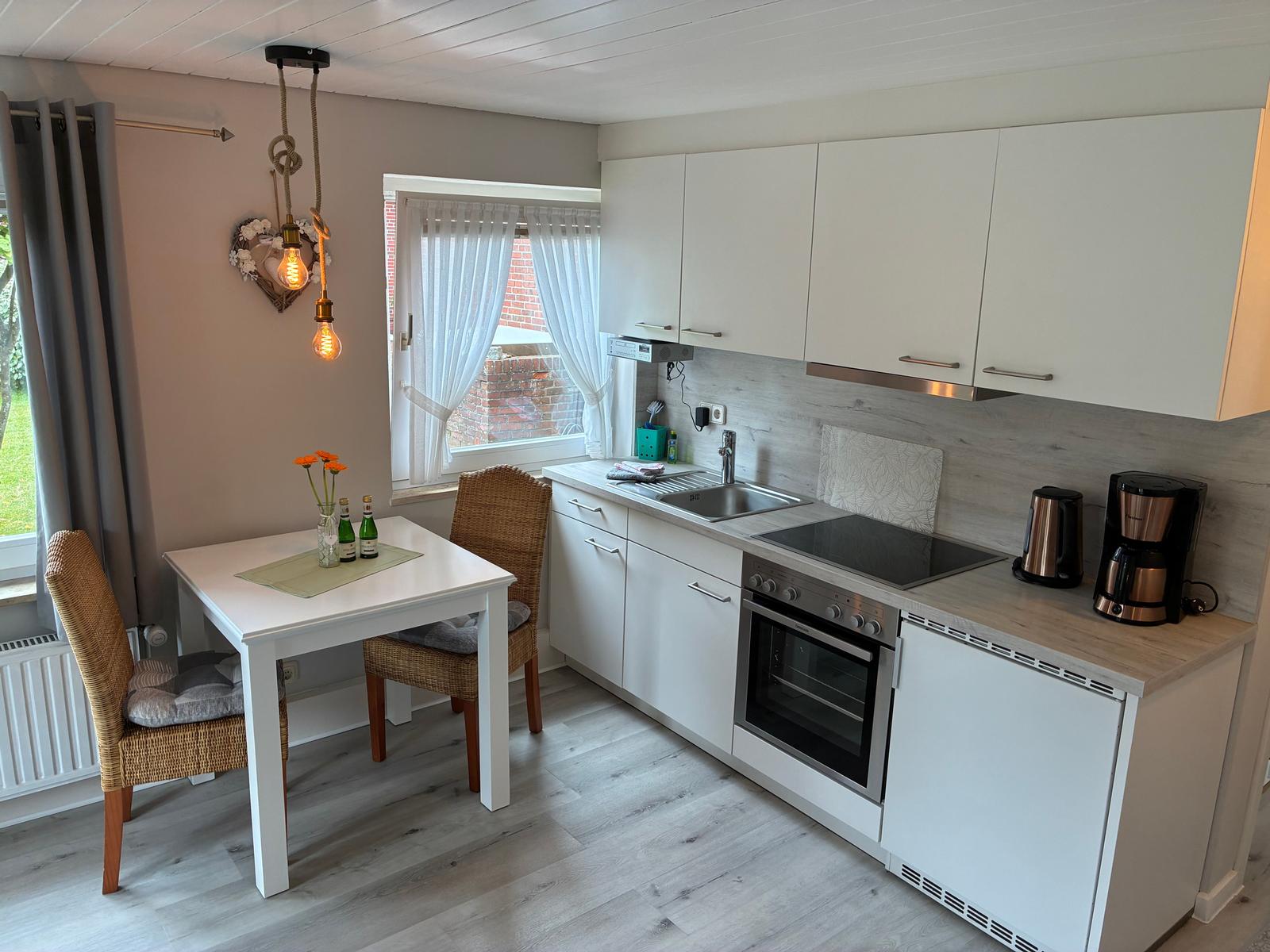 Küche mit Essbereich, weißen Schränken und Holzboden. Fenster mit weißen Vorhängen.