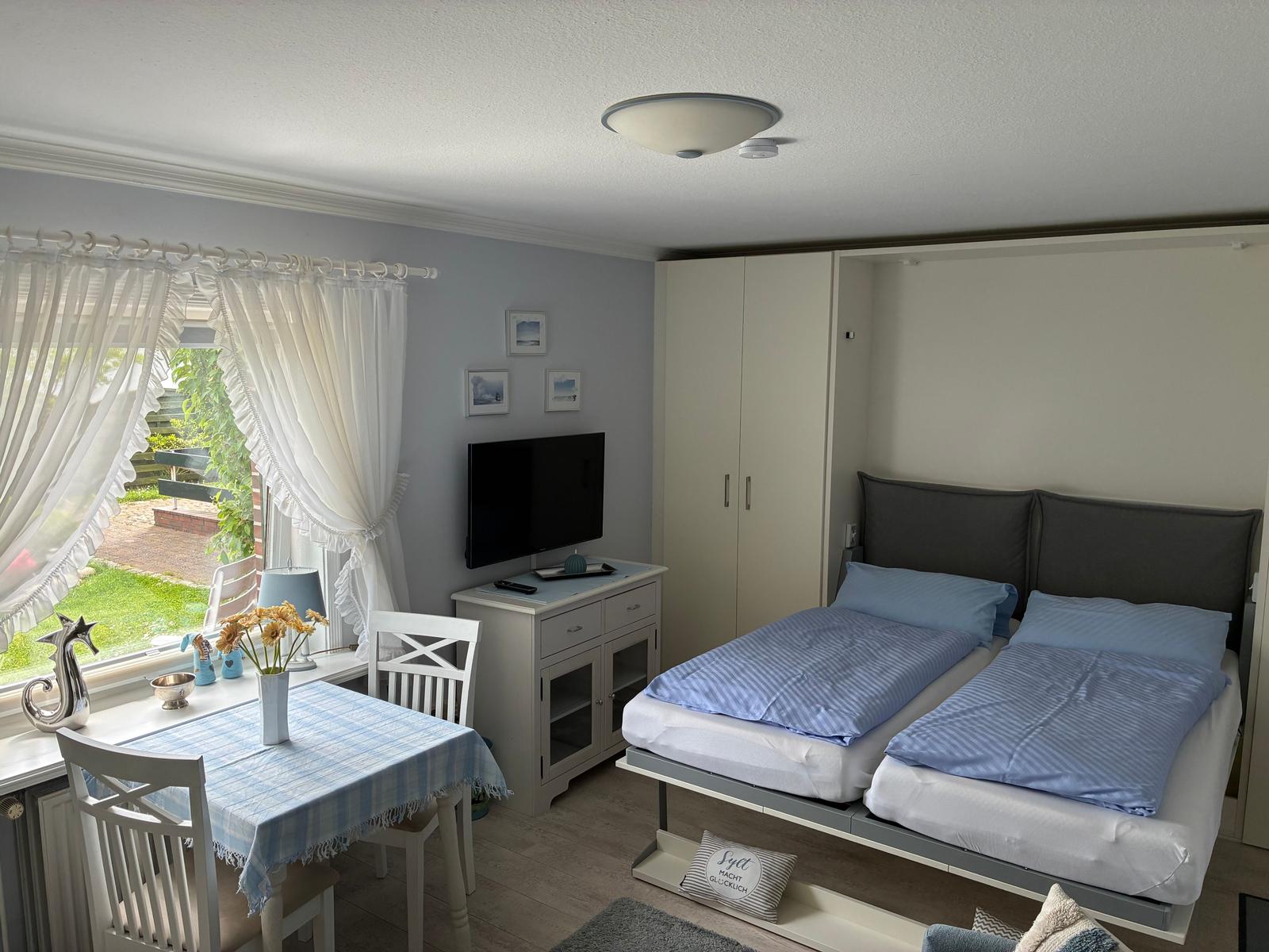 Zimmer mit Schlafplatz, TV und Tisch. Fenster mit Blick auf Garten.