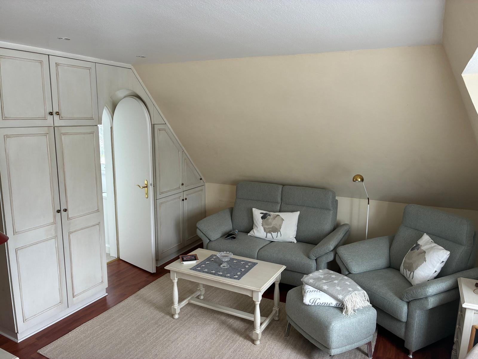 Wohnzimmer mit grauem Sofa, Sessel und Couchtisch unter schrägen Dachschrägen.