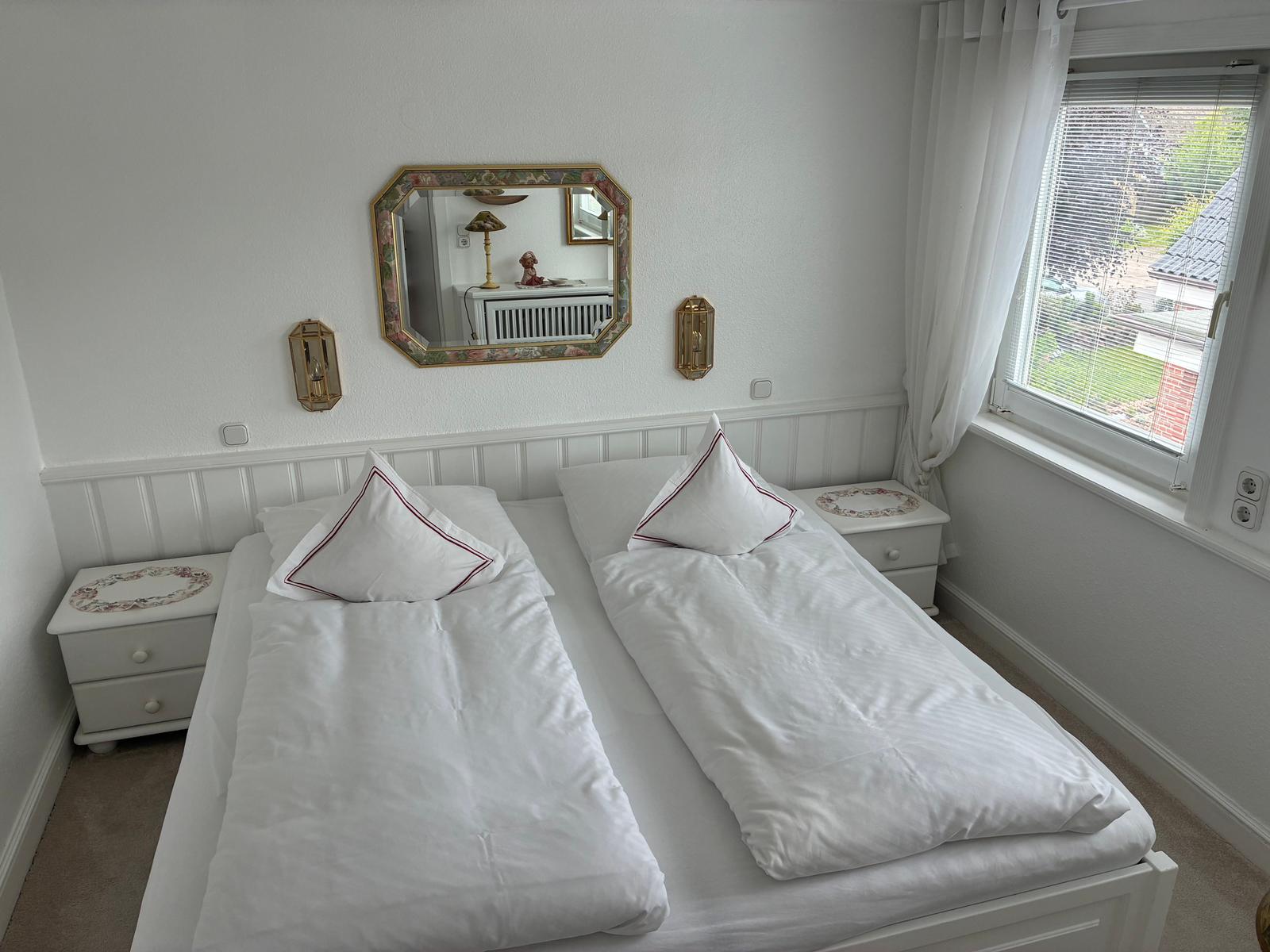 Schlafzimmer mit Doppelbett, zwei Nachttischen und Spiegel an der Wand.