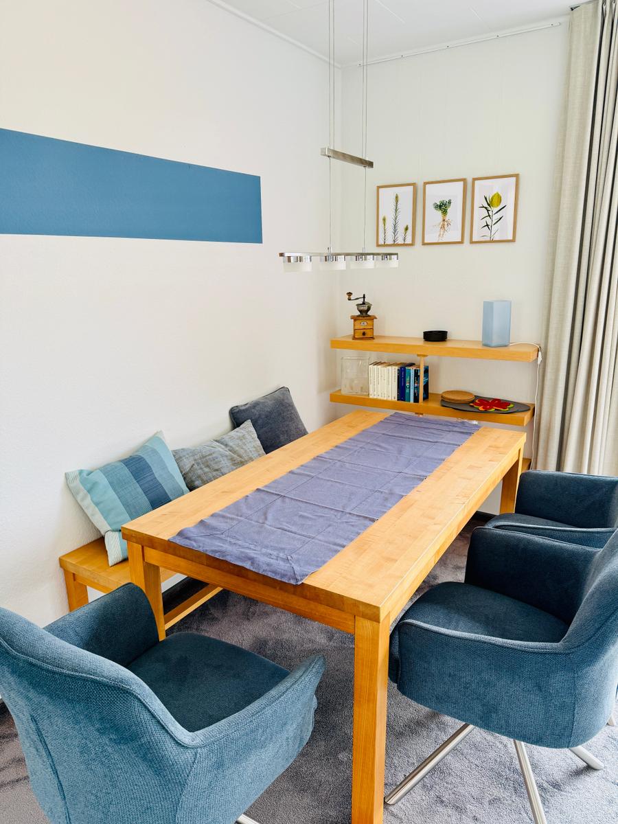 Esszimmer mit Holztisch, blauen Stühlen und Wanddekoration.