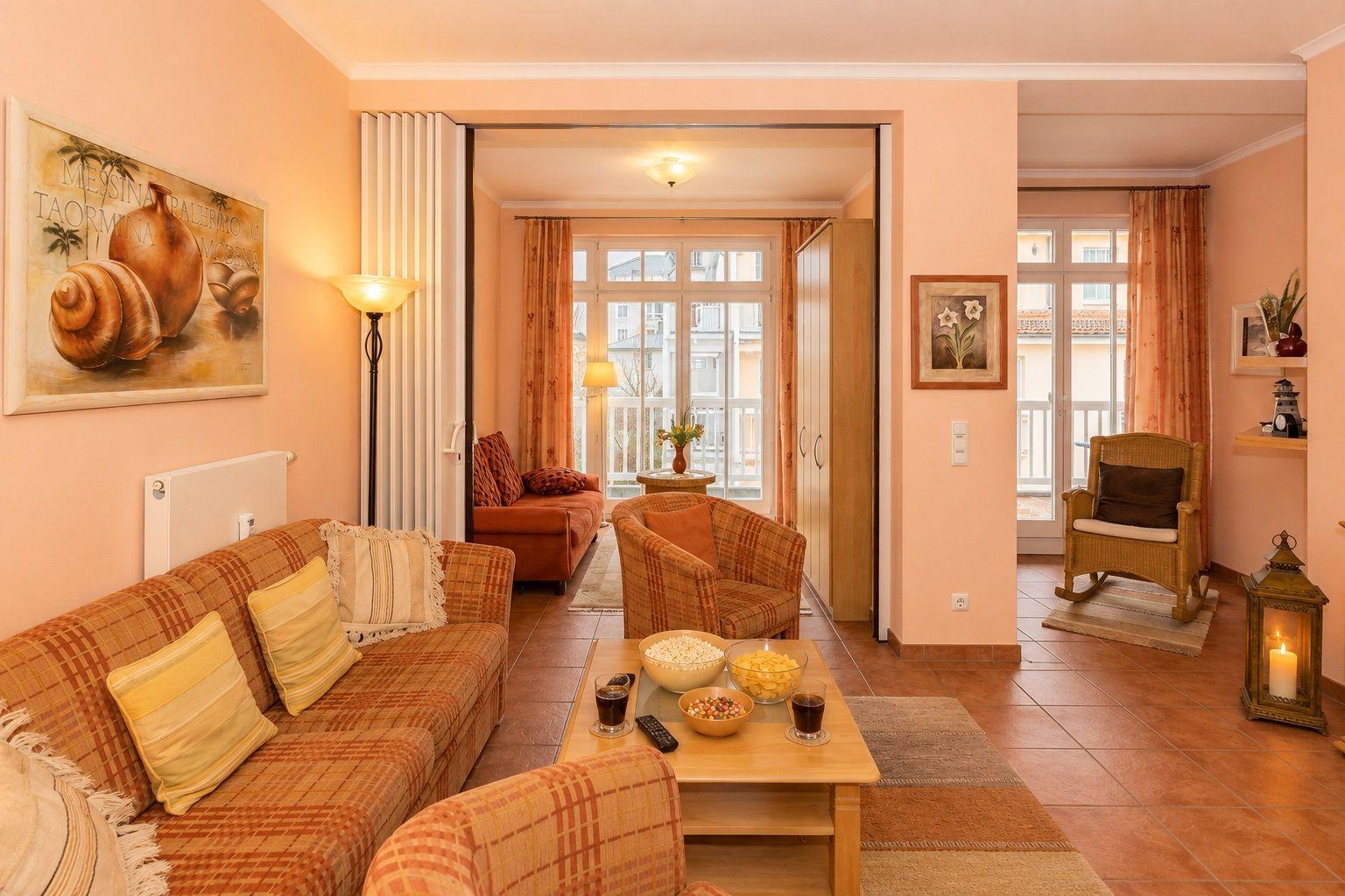 Wohnzimmer mit Sofa, Sessel und Tisch. Durchgang zu Balkon mit Blick.