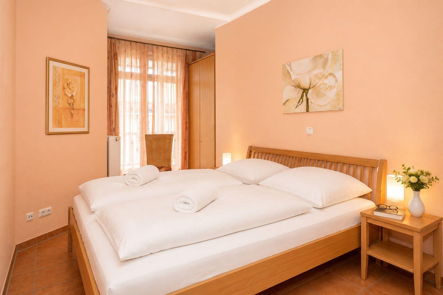 Schlafzimmer mit Doppelbett, Holzmöbeln und Blumenbildern an den Wänden.