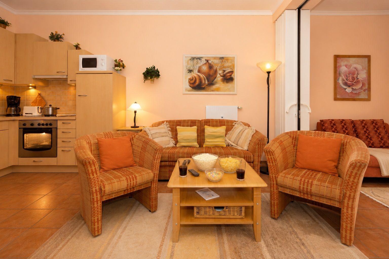 Wohn- und Küchenbereich mit Sofa, Sesseln und Esstisch. Küche mit Herd und Mikrowelle.