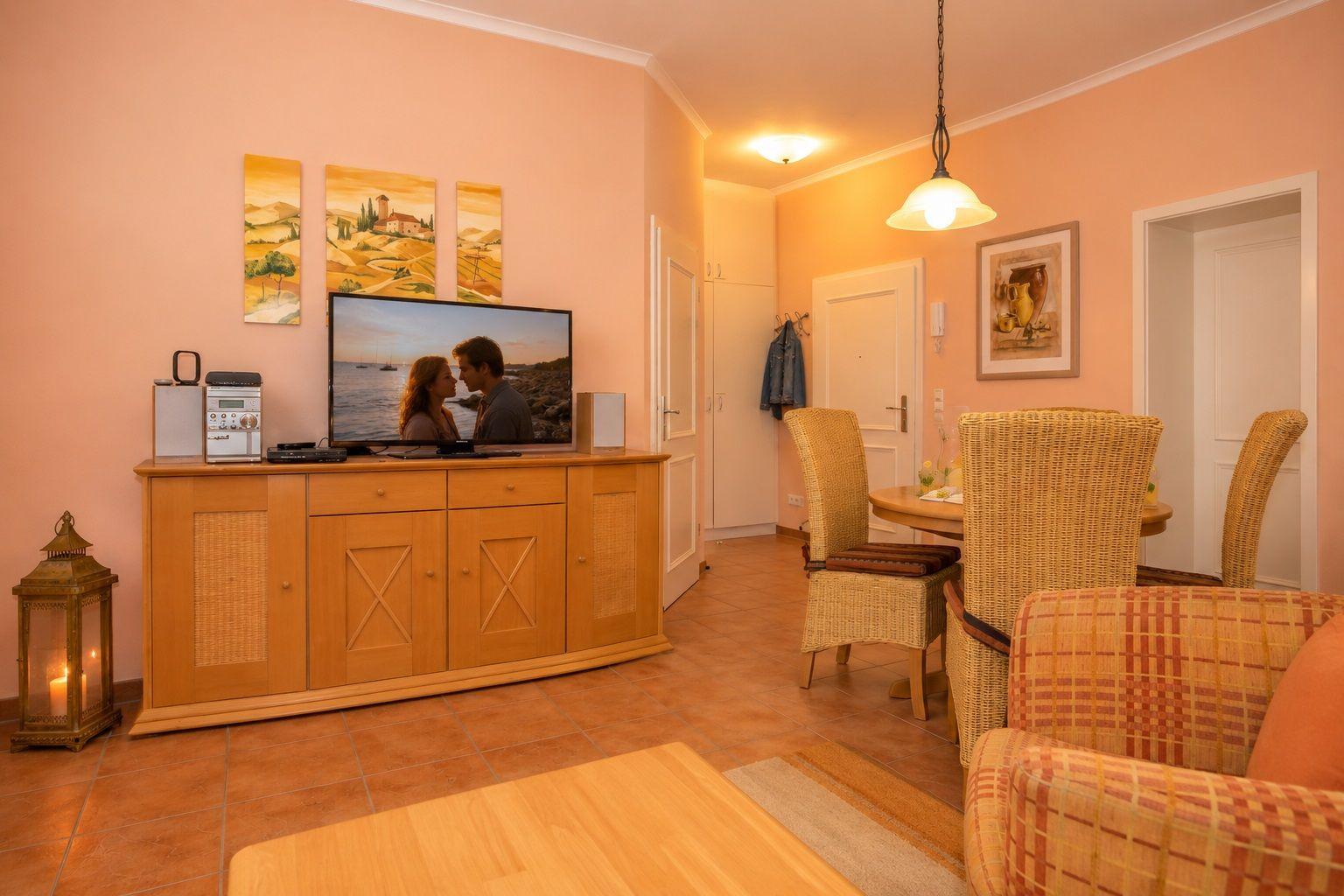 Wohn- und Essbereich mit TV, Esstisch und Sessel. Wandbild und Beleuchtung sichtbar.