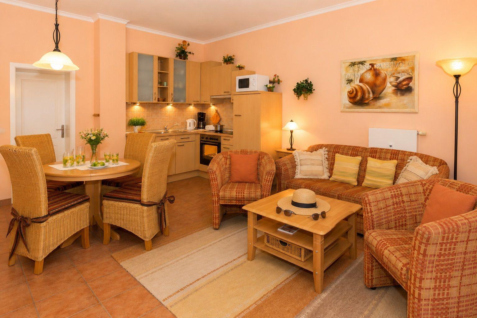 Wohnküche mit Esstisch, Sofa und Küchenzeile. Wandbild und Pflanzen sind sichtbar.