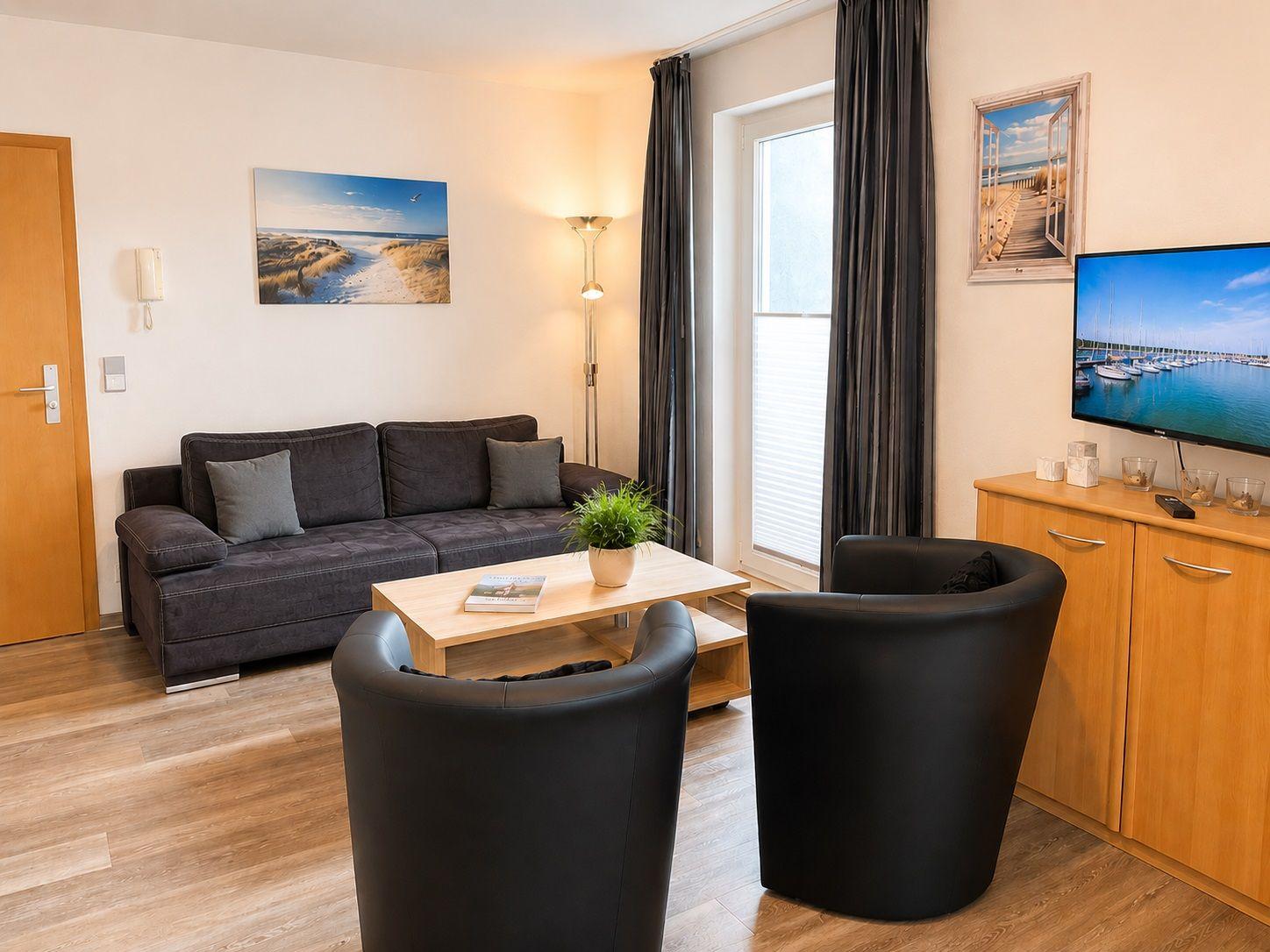 Wohnzimmer mit Sofa, zwei Sesseln, Couchtisch und Fernseher.
