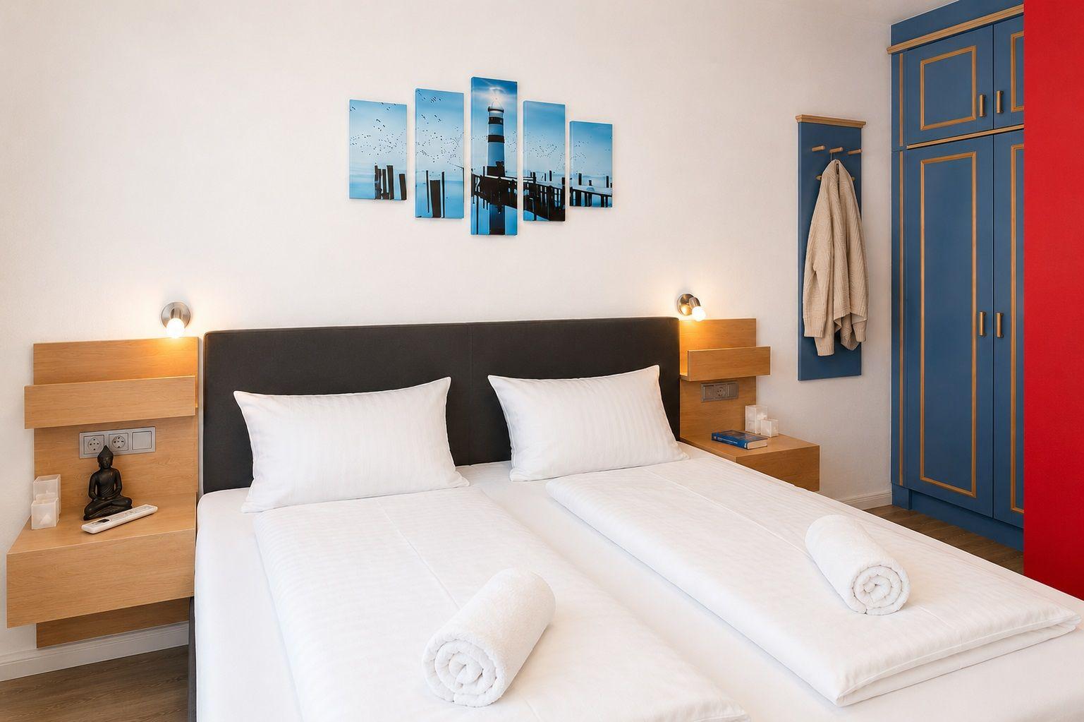 Schlafzimmer mit Doppelbett, blauem Schrank und Wandbild mit Leuchtturm.