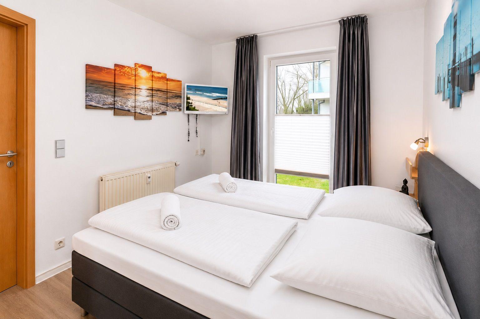 Schlafzimmer mit Doppelbett, Fenster, Wandbild und Fernseher.