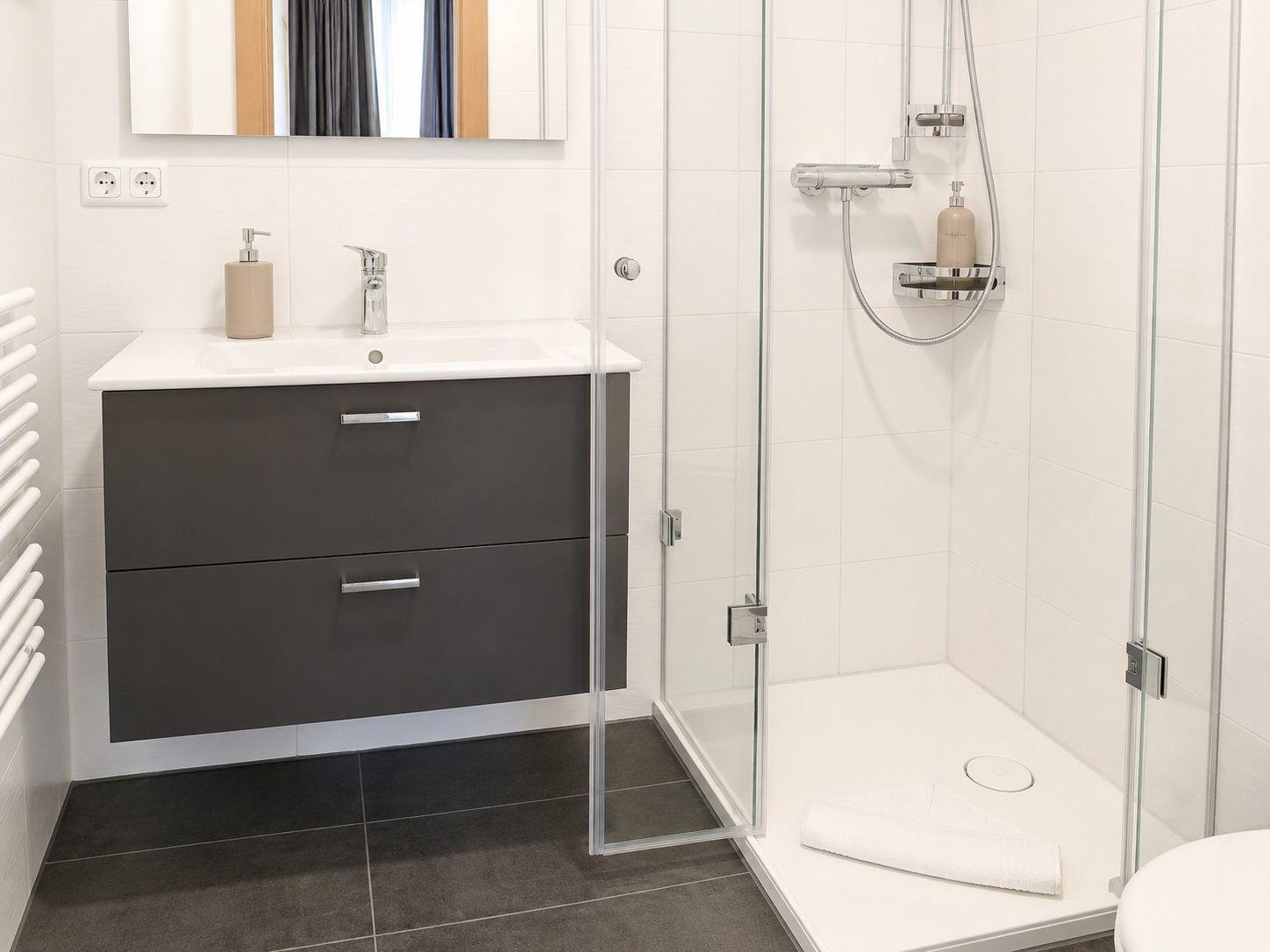 Badezimmer mit Dusche, Waschbecken und Spiegel. Fliesen und moderne Einrichtung.