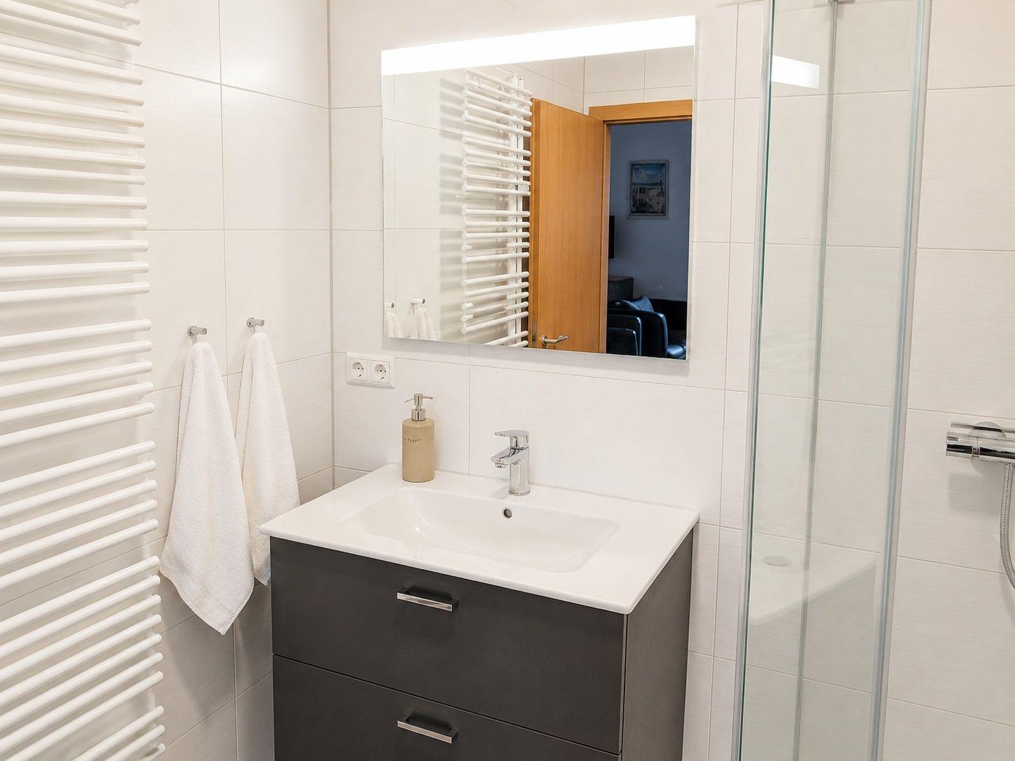 Badezimmer mit Waschbecken, Spiegel, Dusche und Heizung.