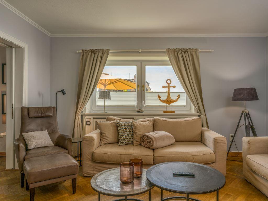 Wohnzimmer mit Sofa, Sessel und Fenster mit Blick auf Terrasse.