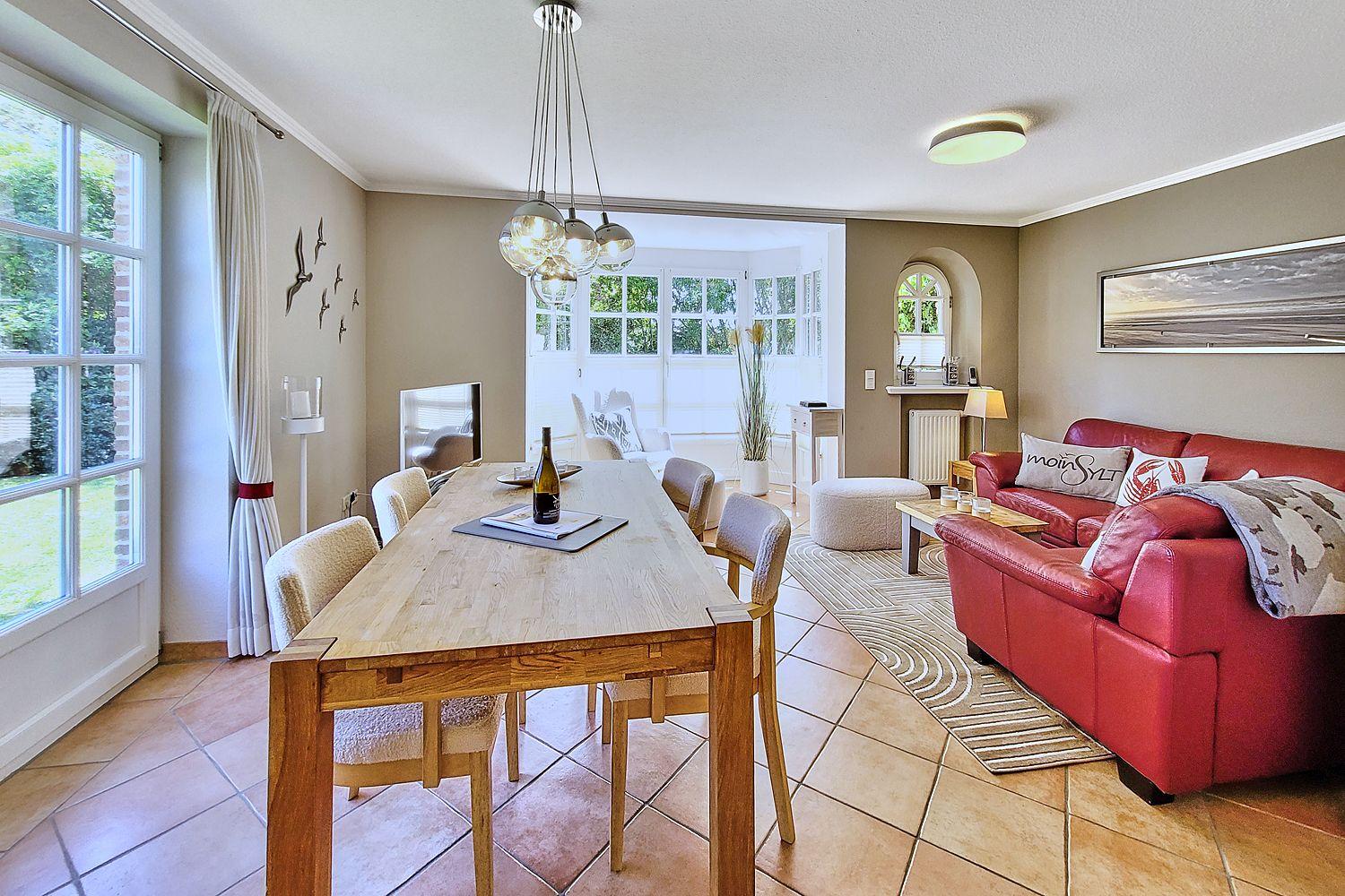 Essbereich mit Holztisch und rotem Sofa im Wohnzimmer. Große Fenster und moderne Beleuchtung.