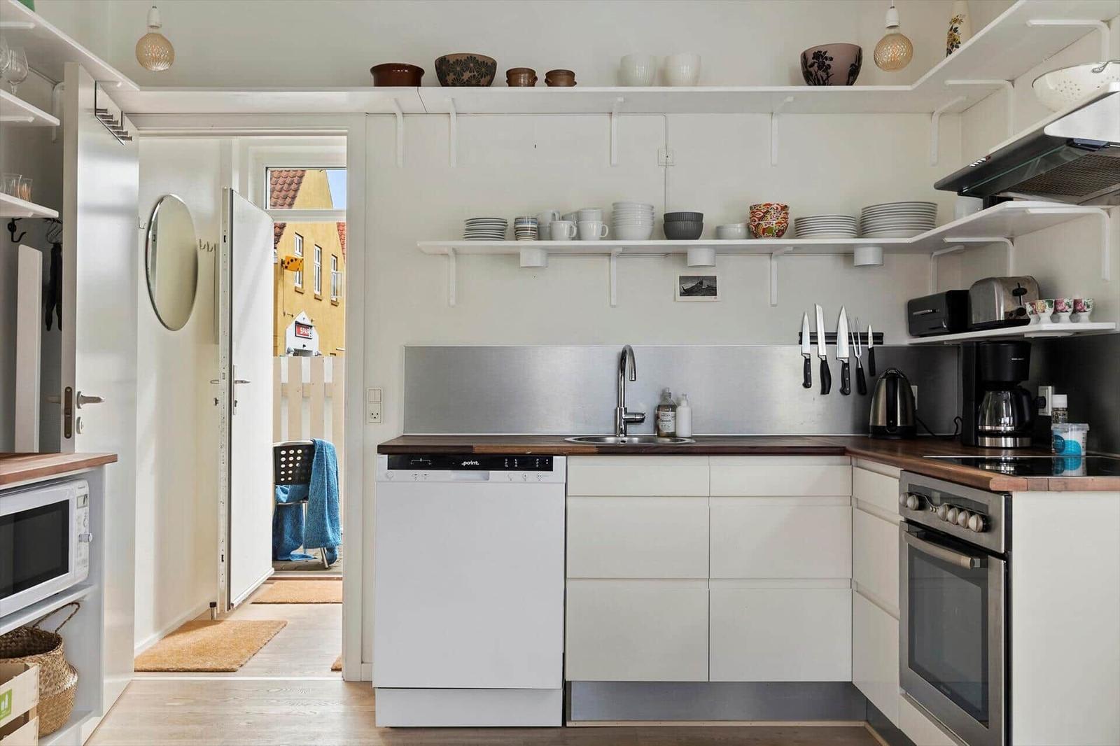 Kitchen with white cabinets, stainless steel sink, and open shelves with dishes.