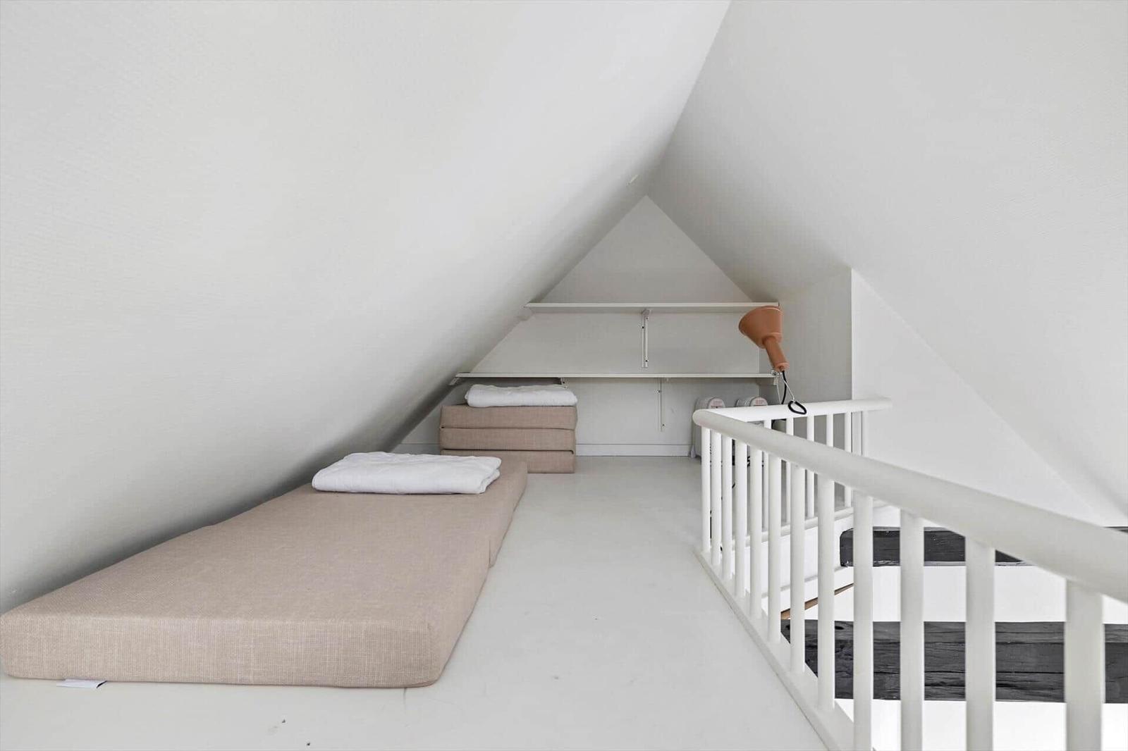 Room with two mattresses and white staircase in attic.