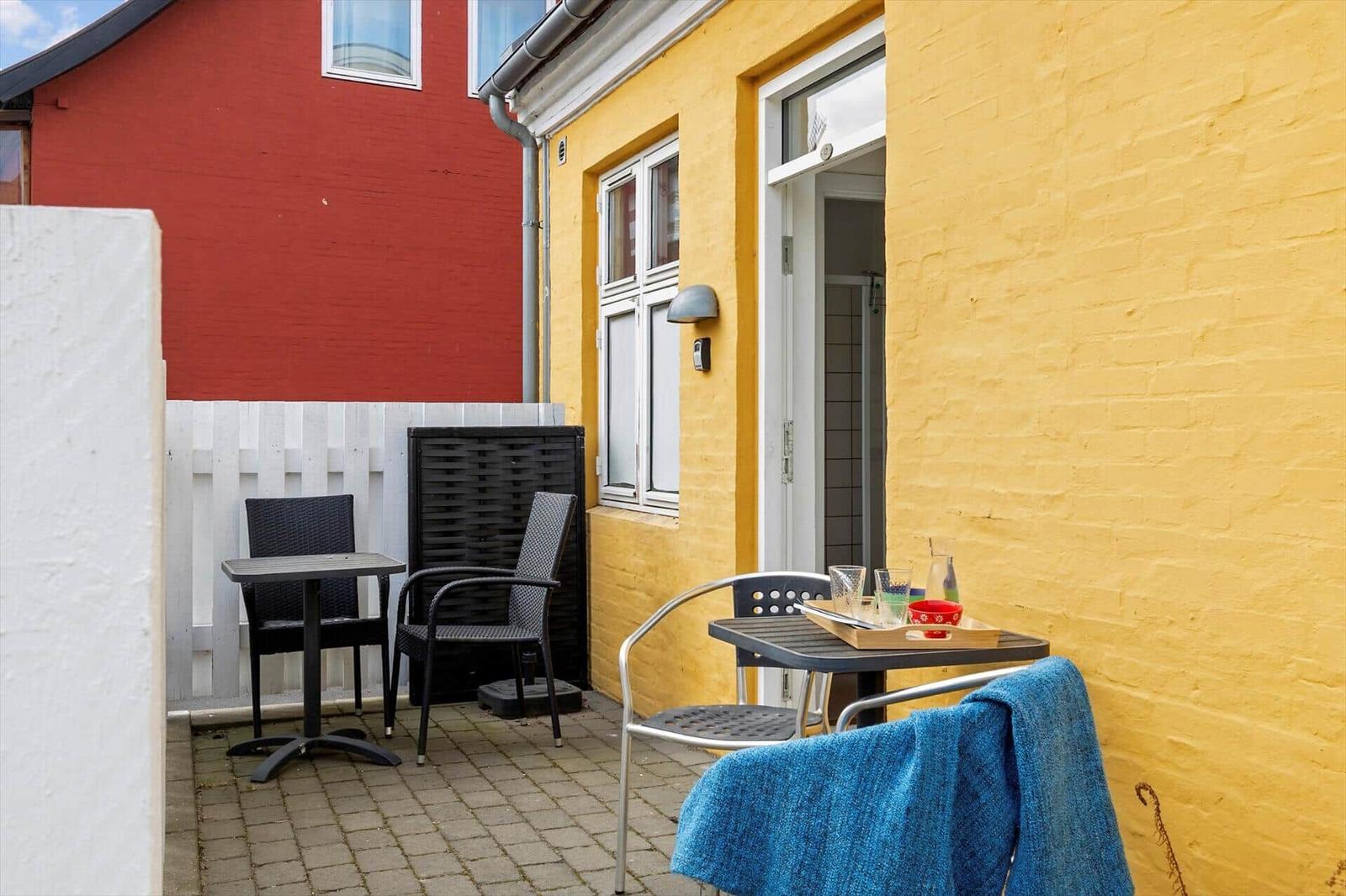 Terrace with table, chairs, and blue towel against yellow house wall.