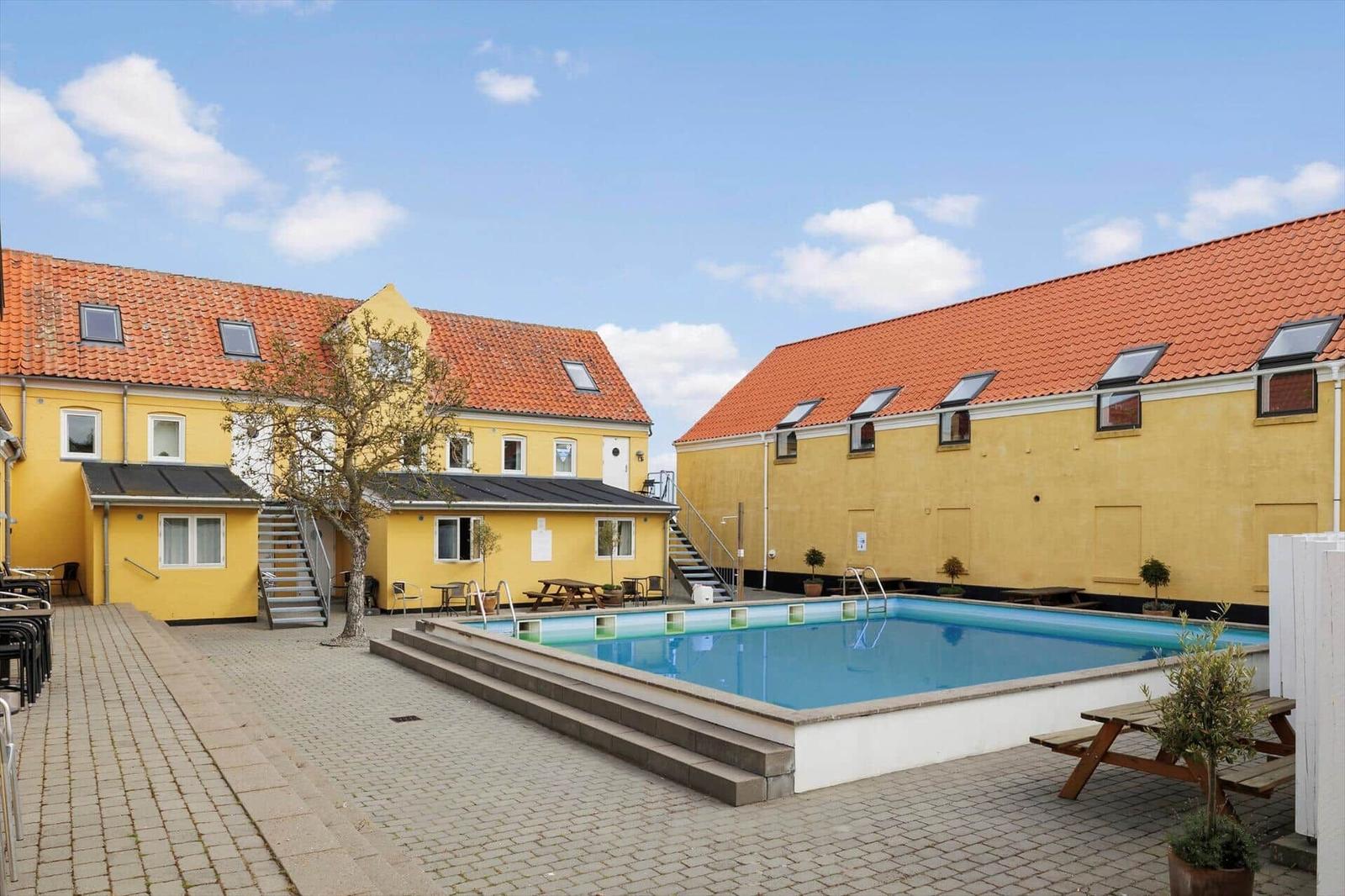 Pool area with yellow buildings and patio furniture.