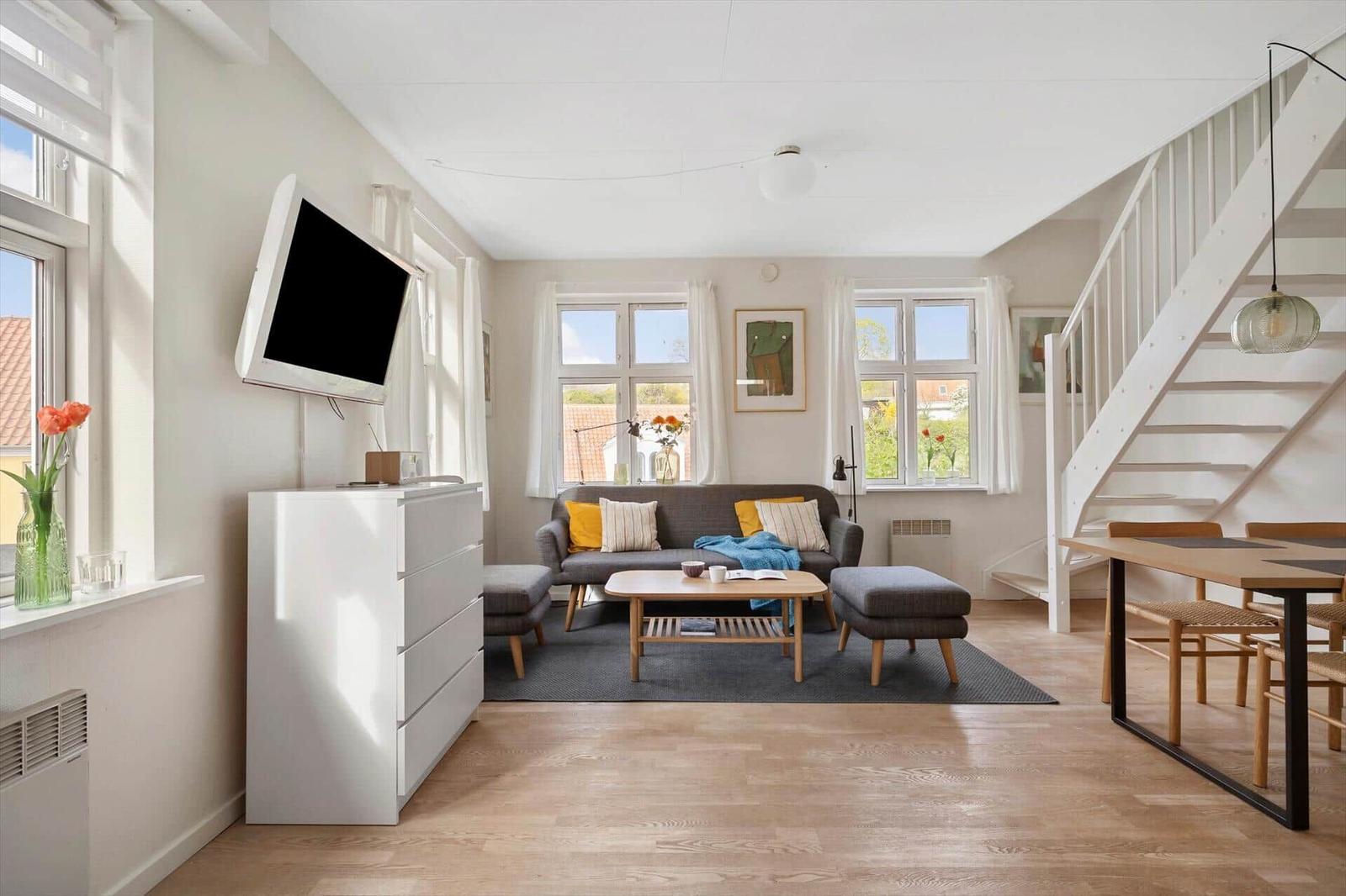 Living room with sofa, coffee table, and TV. Wooden floor and windows with view.