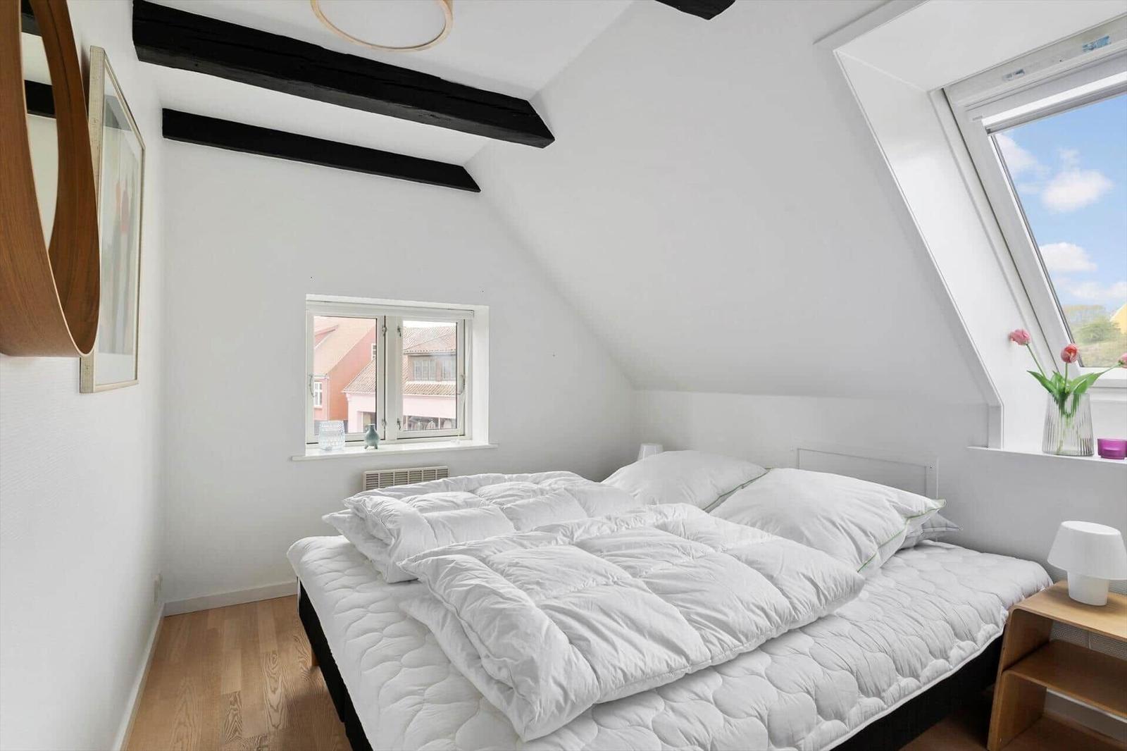 Bedroom with skylight, bed and wooden floor. A mirror hangs on the wall.