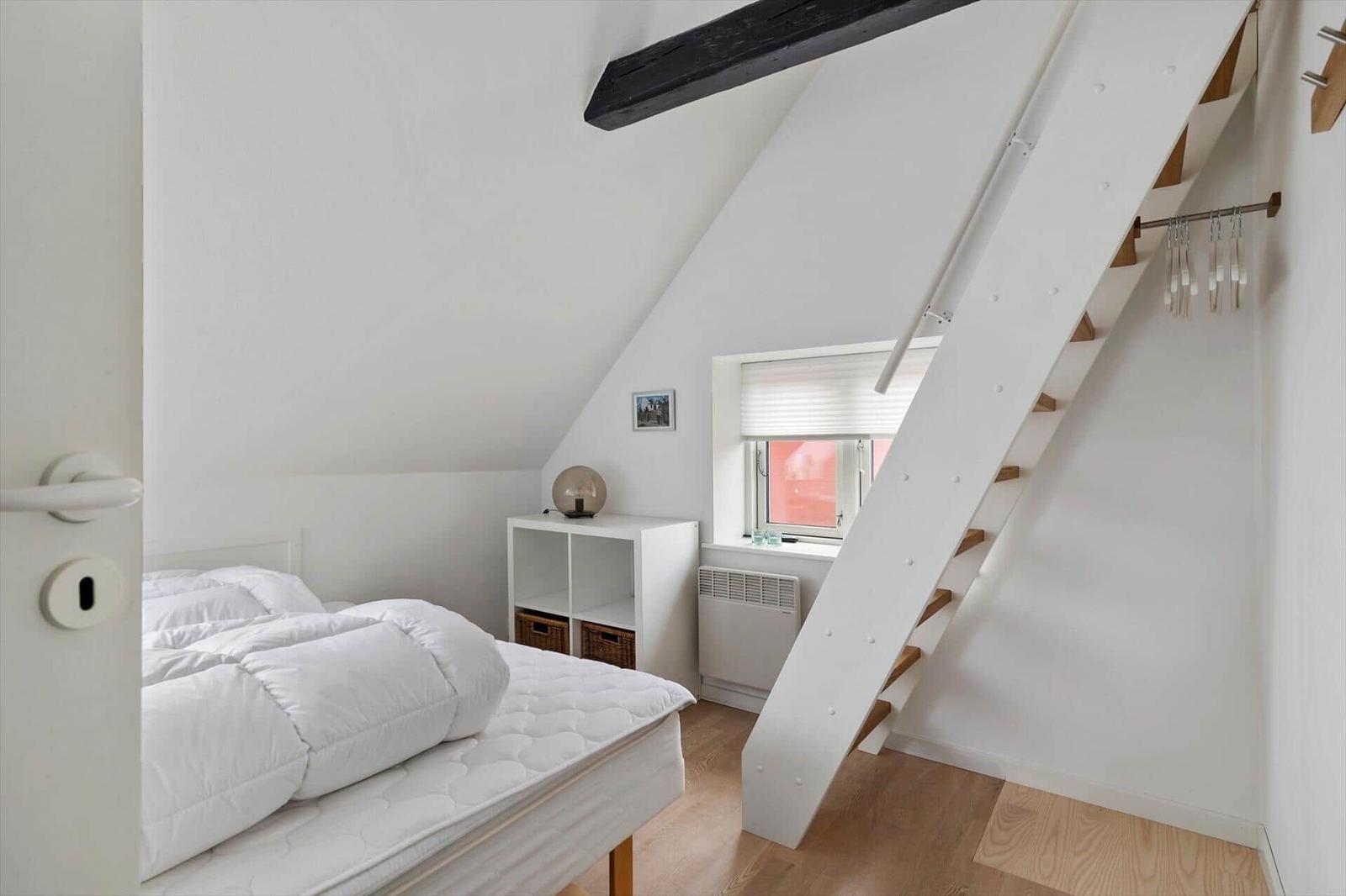 Bedroom with sloped ceiling, bed, window, and stairs.