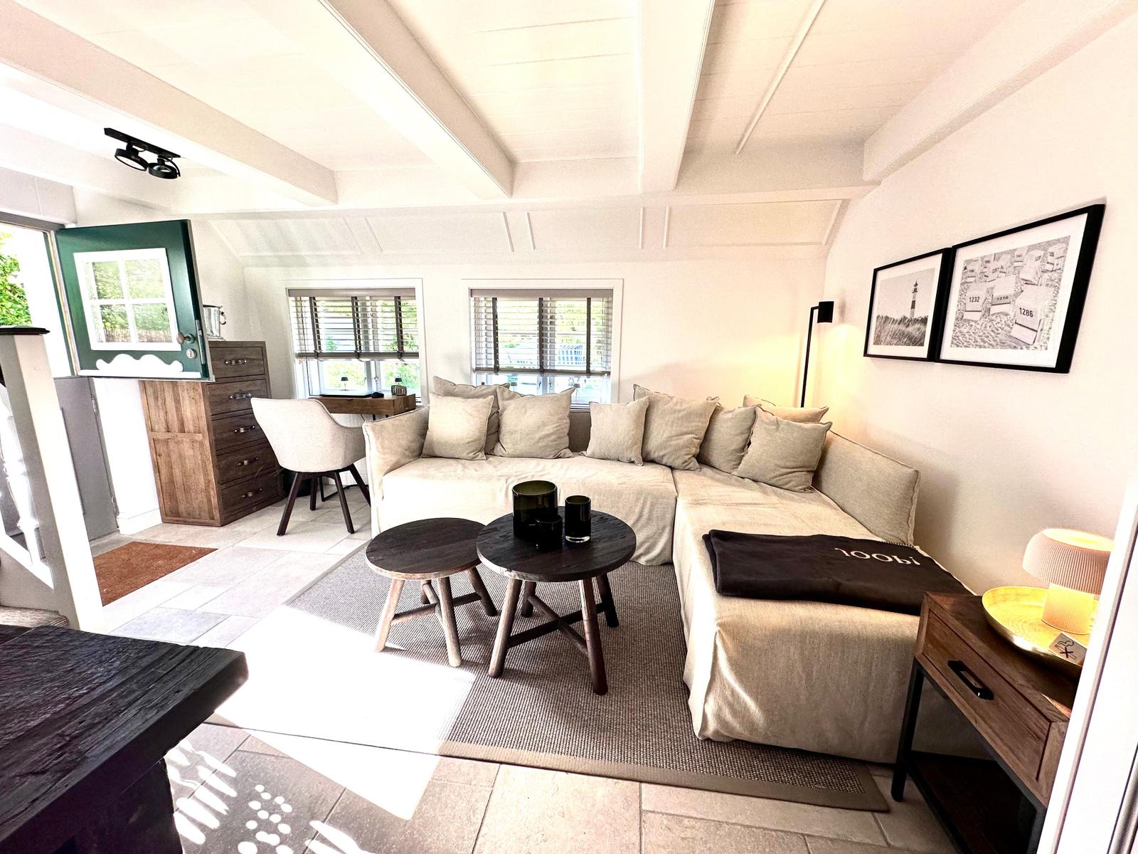 Wohnzimmer mit Sofa, Tischen und Fenstern. Holzmöbel und Wandbilder.