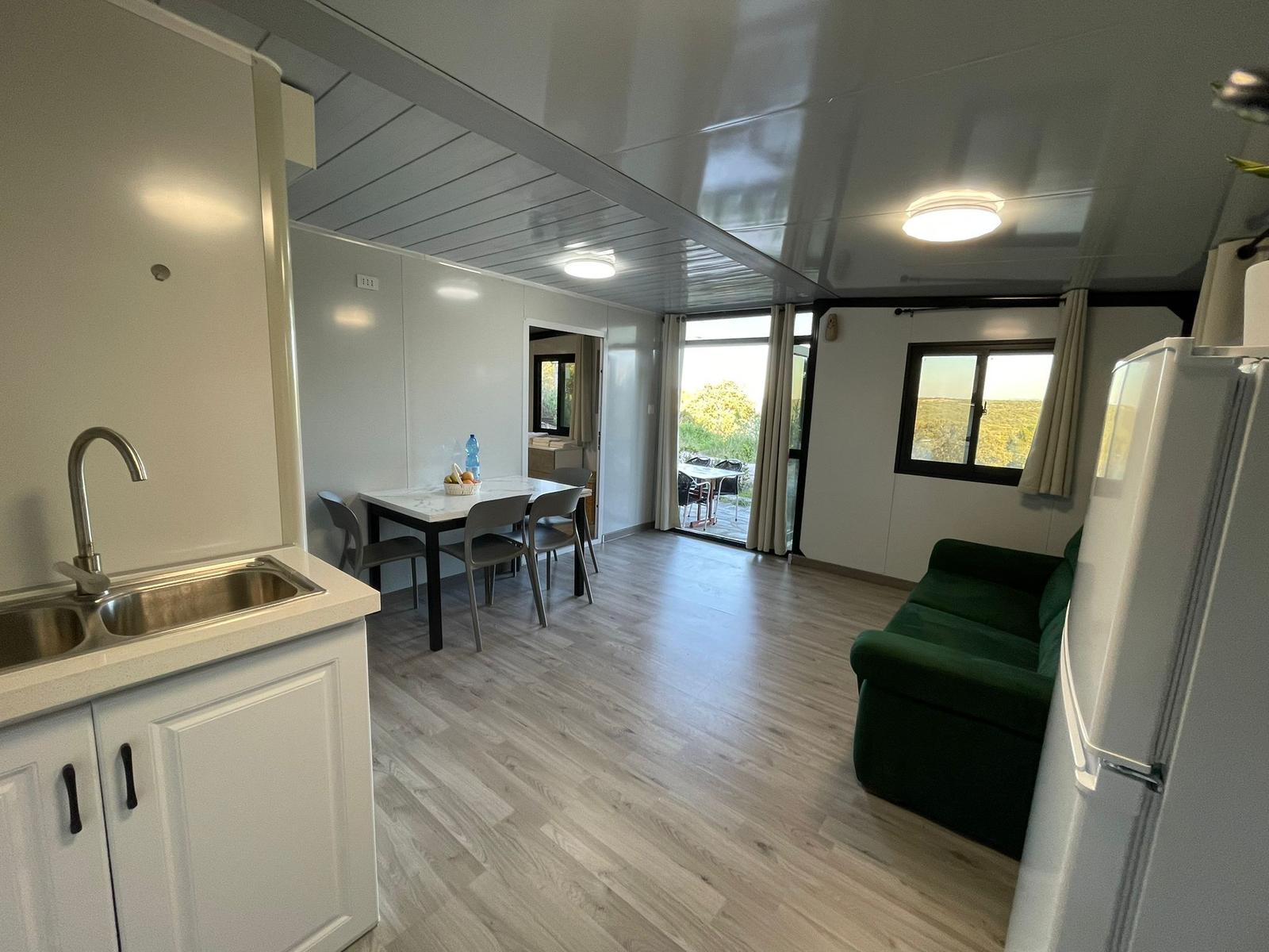 Kitchen with sink, dining table, sofa, and refrigerator. Passage to terrace with view of green areas.
