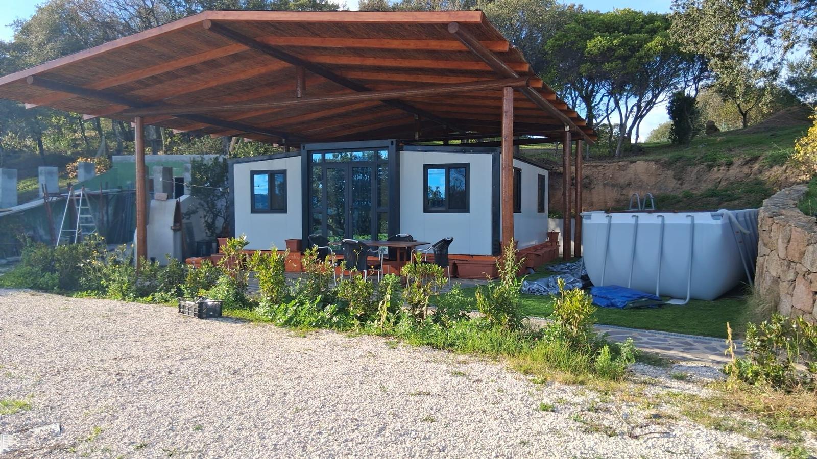 Modern accommodation with covered terrace, table, chairs, and pool in background.