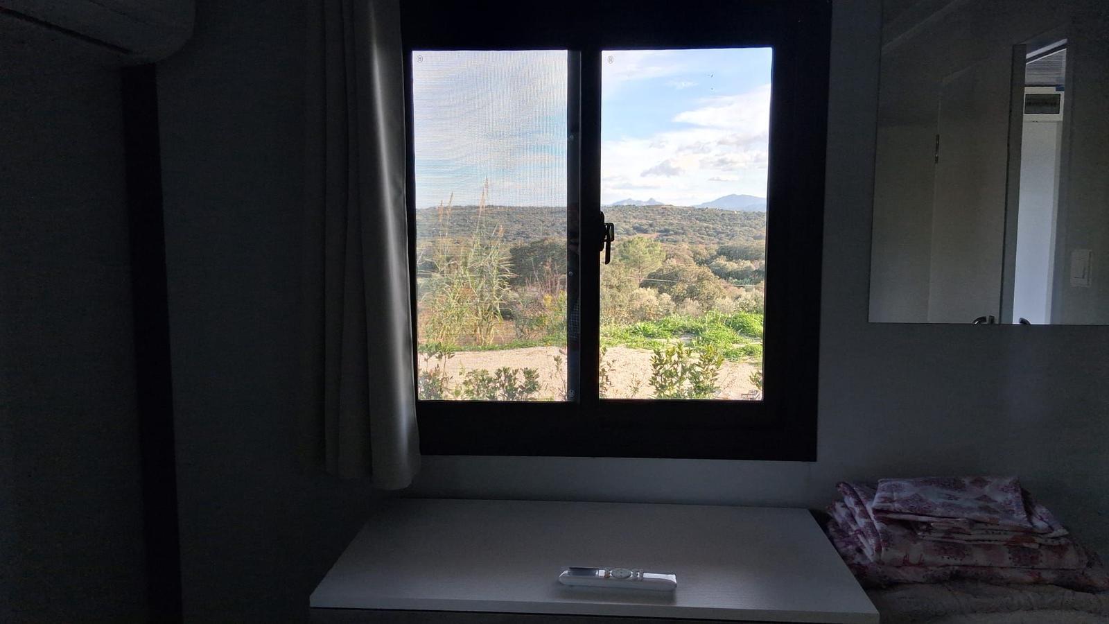 Through the window, you see a hilly landscape with trees and mountains in the background.