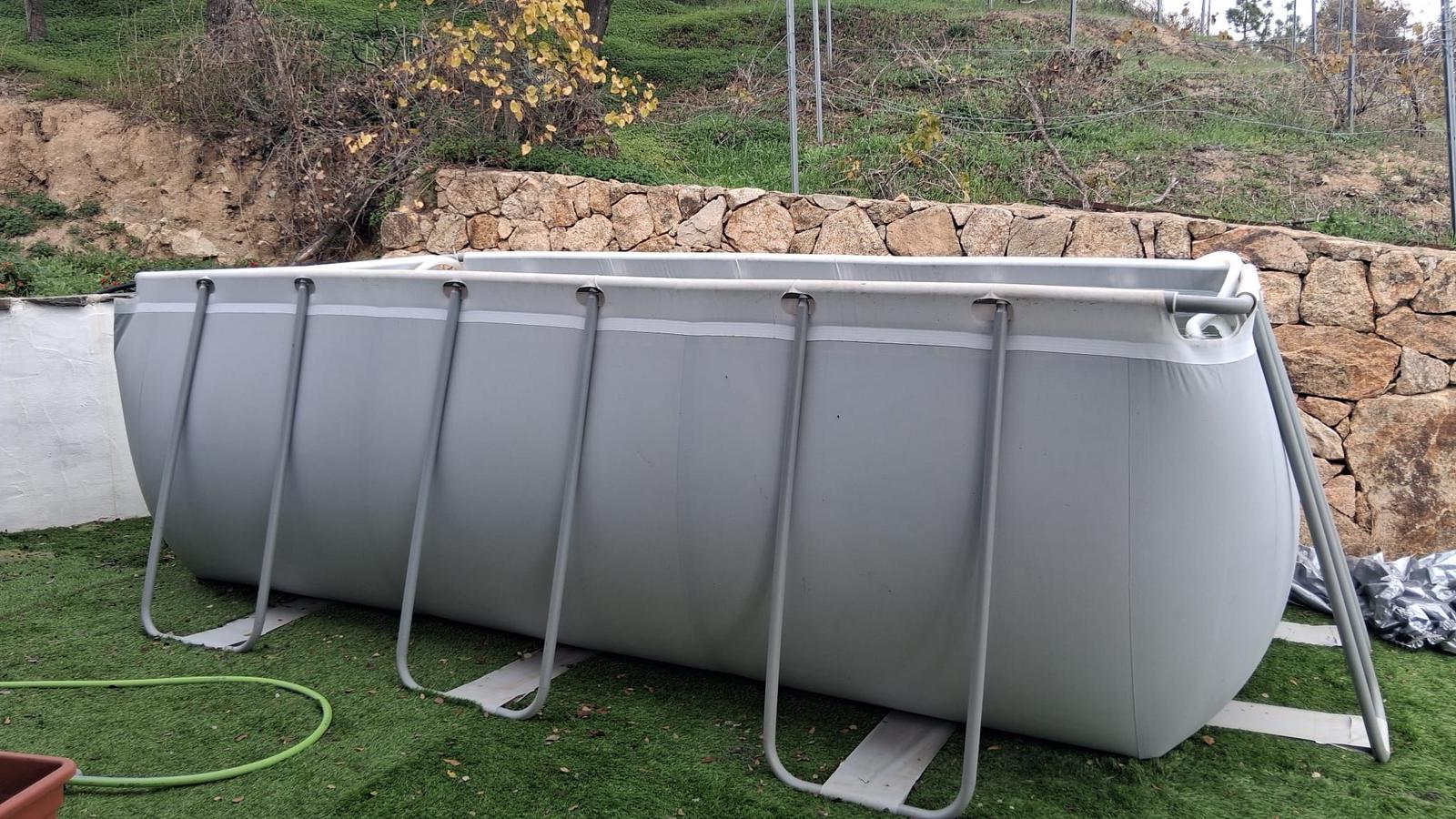 An inflatable pool sits on artificial grass in front of a stone wall.