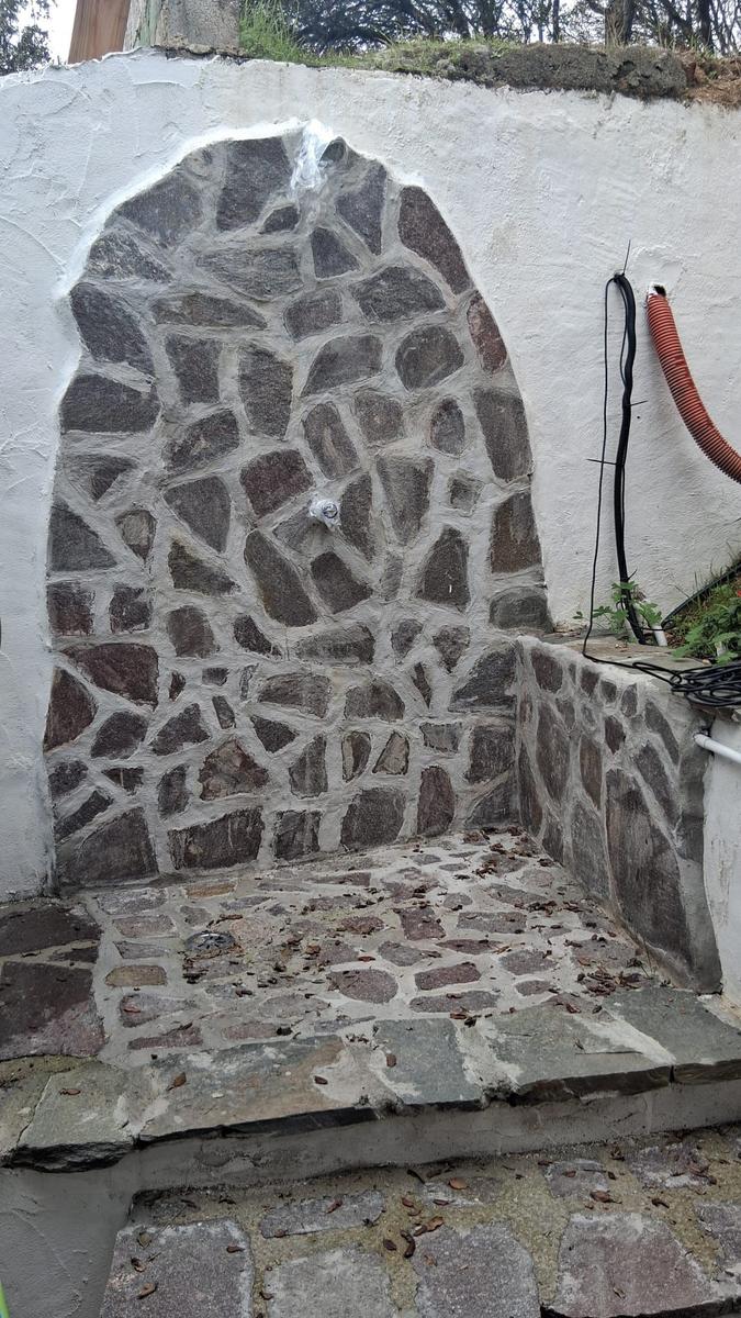 Stone shower with arched design and faucet on the wall.
