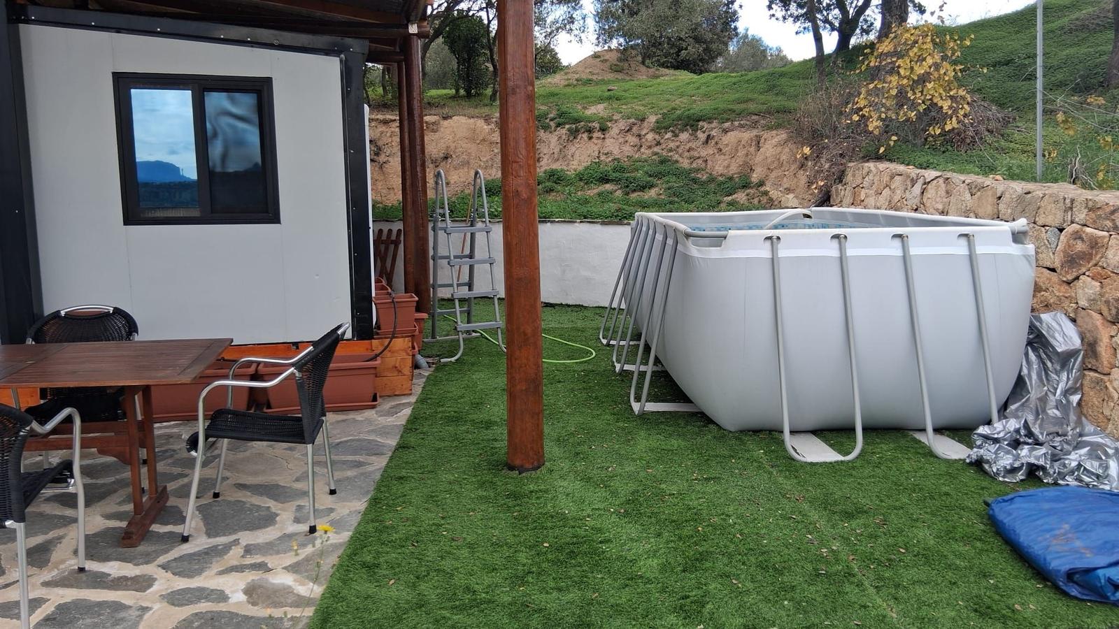 Outdoor area with pool, table and chairs on stone and artificial grass.