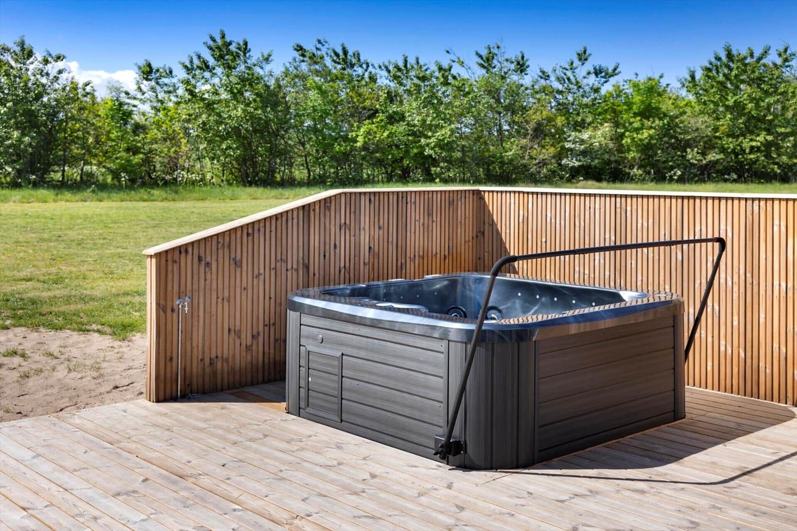 Ein Whirlpool auf einer Holzterrasse mit Holzgeländer und Grünfläche im Hintergrund.