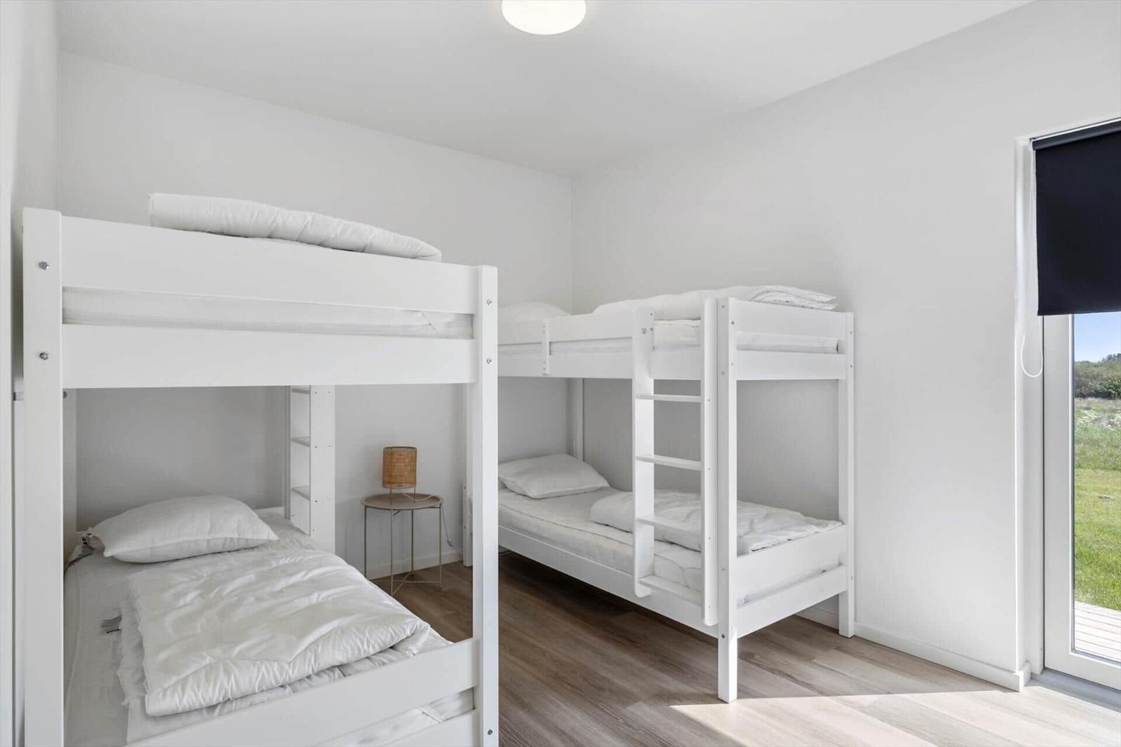 Zwei weiße Doppelstockbetten mit weißen Bettwäsche und einem Nachttisch mit Lampe.