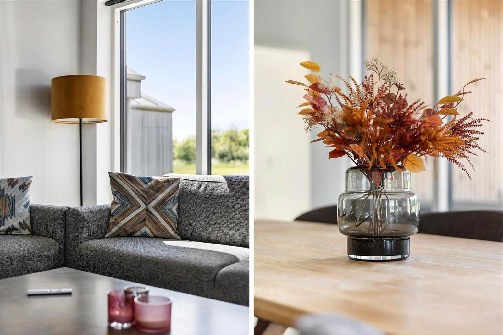 Ein grauer Sofa mit Kissen und ein Tisch mit Blumen in einem Glasvasen.