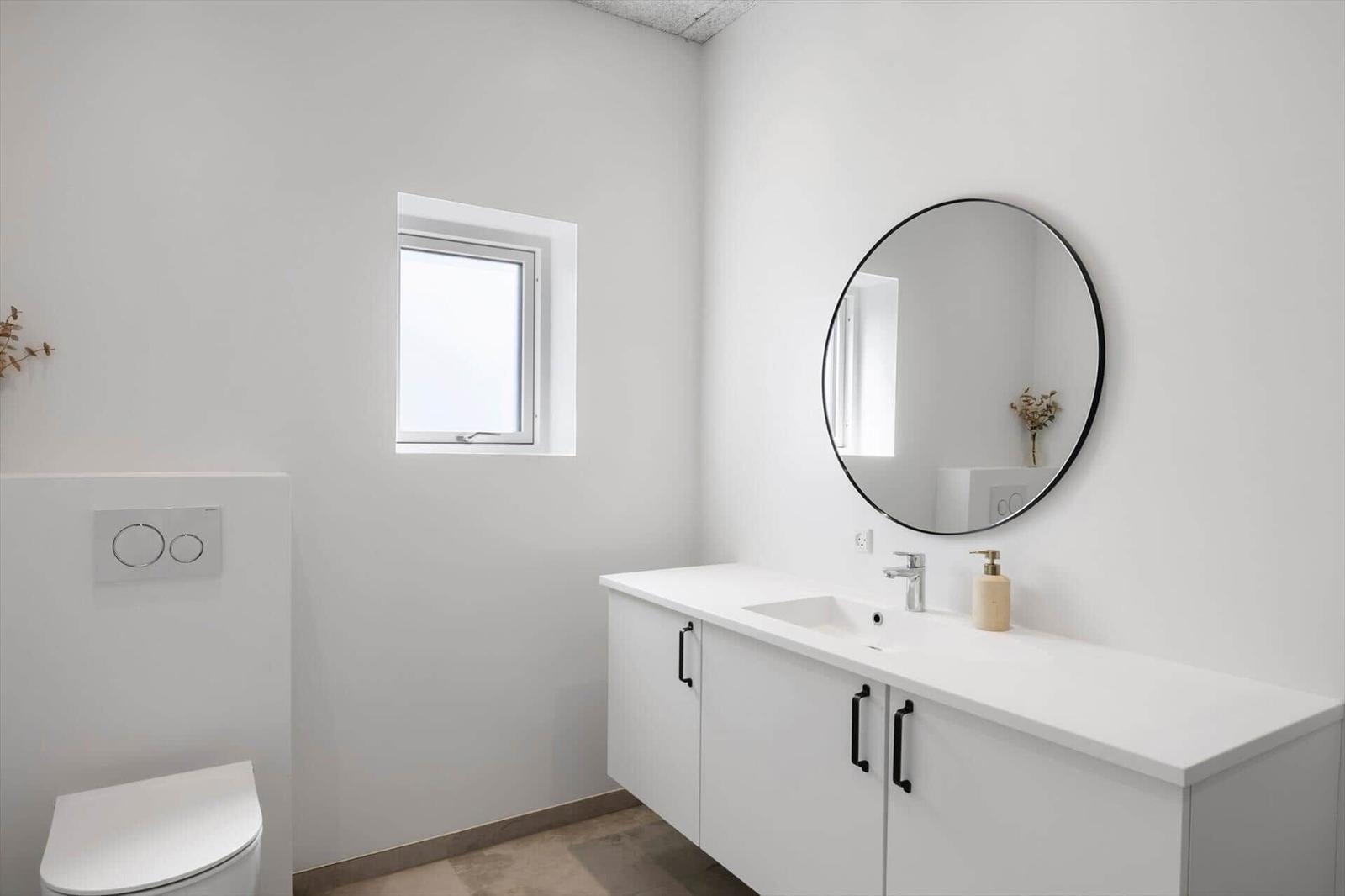 Badezimmer mit Waschbecken, Spiegel und Toilette. Fenster sorgt für Tageslicht.