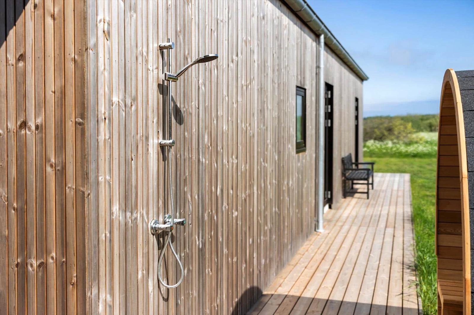Außen-Dusche an Holzhauswand mit Terrasse und Sitzgelegenheit.