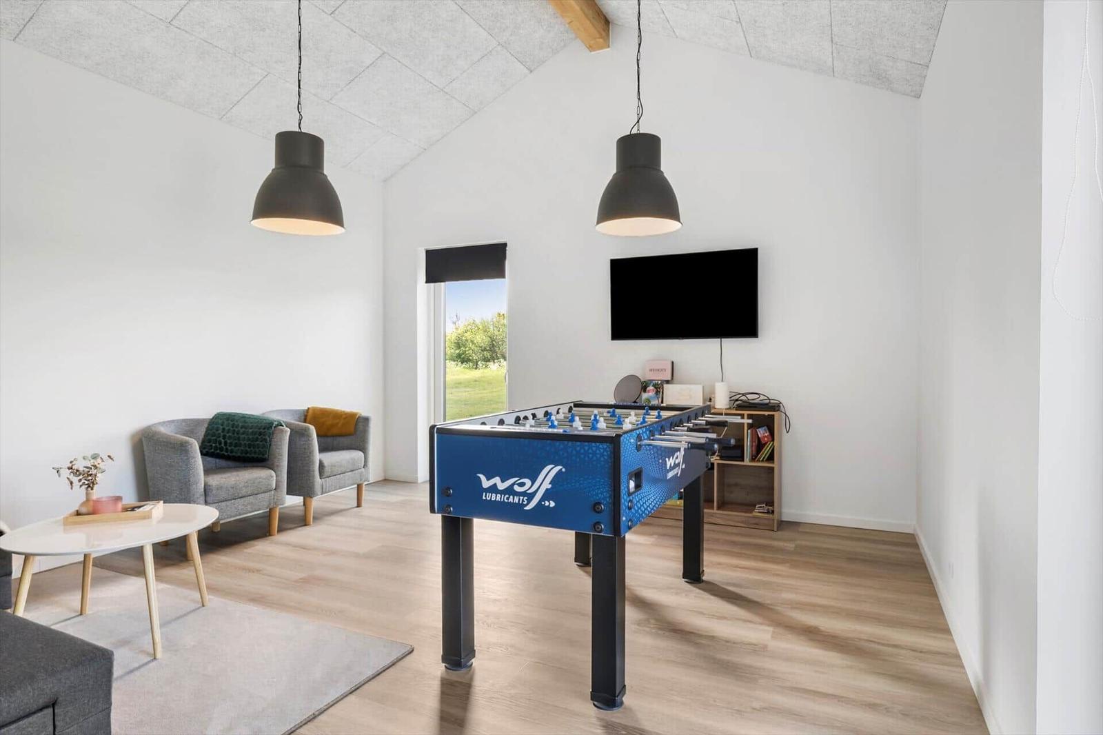 Raum mit Tischfußball, Sofa und Fernseher. Holzboden und helle Wände.