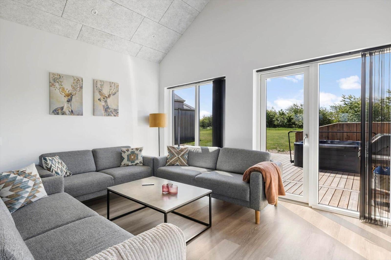Wohnzimmer mit grauem Sofa, Couchtisch und Blick auf die Terrasse mit Whirlpool.