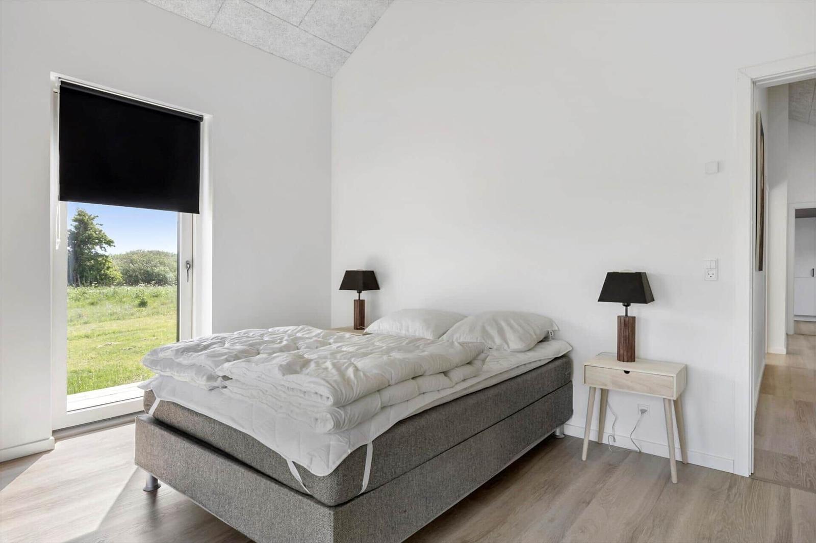 Schlafzimmer mit Bett, Nachttischen und Fenster zum Grün.