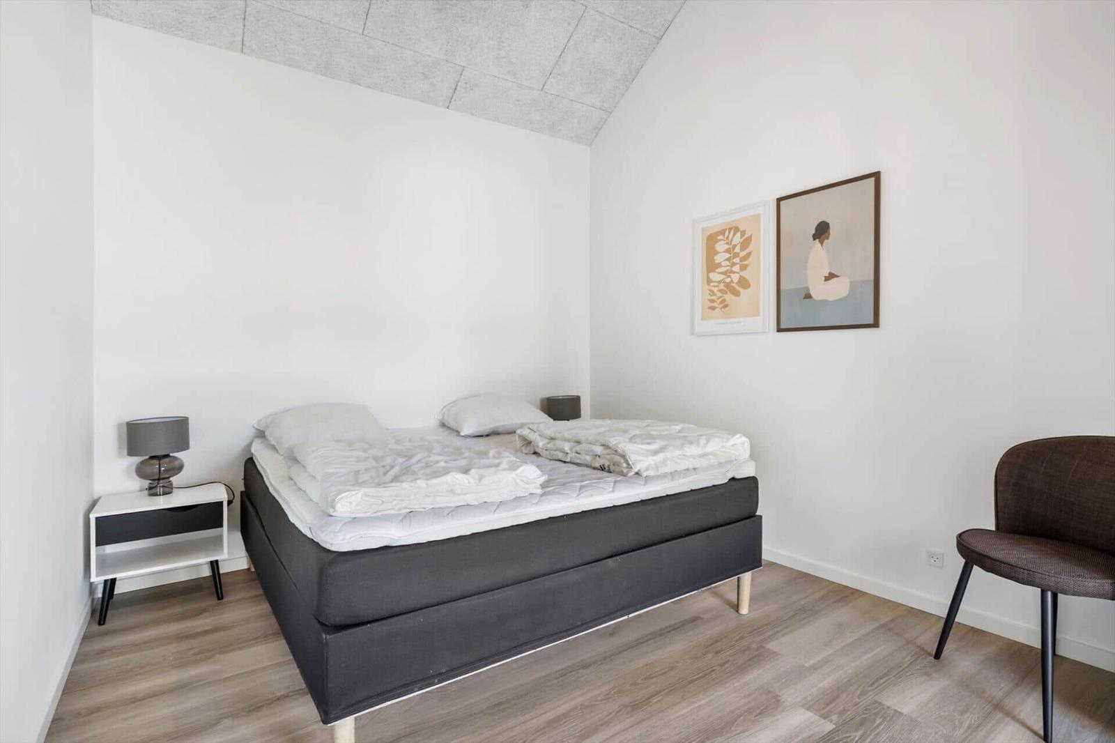 Schlafzimmer mit Bett, Nachttisch, Stuhl und Wandbildern.