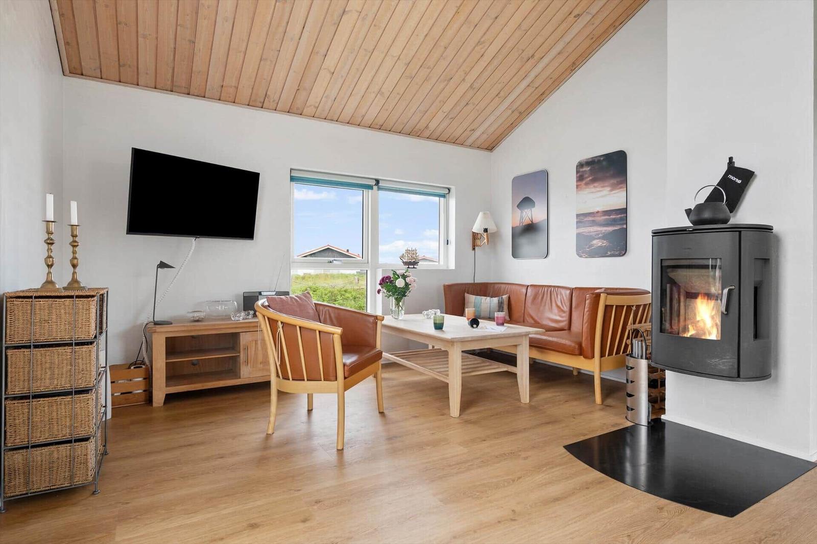 Living room with wooden ceiling, sofa, TV, and wood stove.