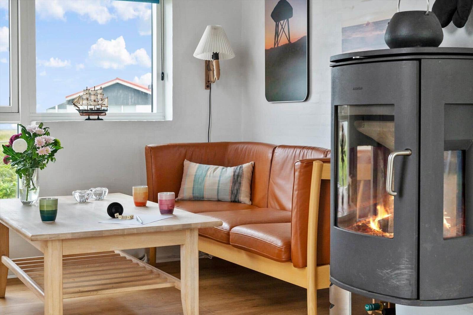 A living room with leather sofa, wood stove, and table with vases and glasses.
