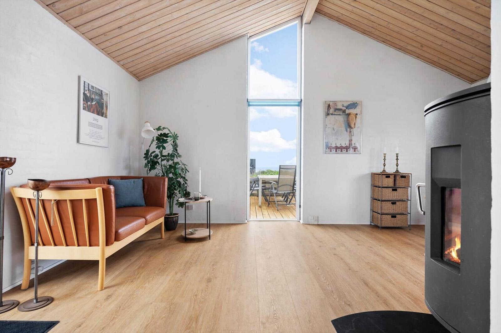 A living room with wooden ceiling, sofa, fireplace, and view to the terrace.