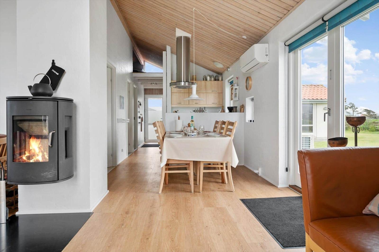 Dining area with table and chairs, wood stove, and large window with view.
