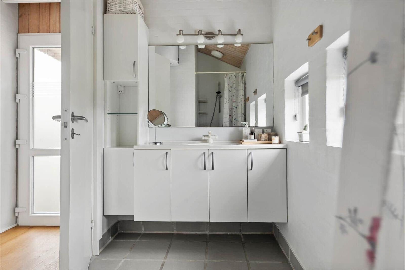Bathroom with white sink, mirror cabinet, and shower. Door leads outside.