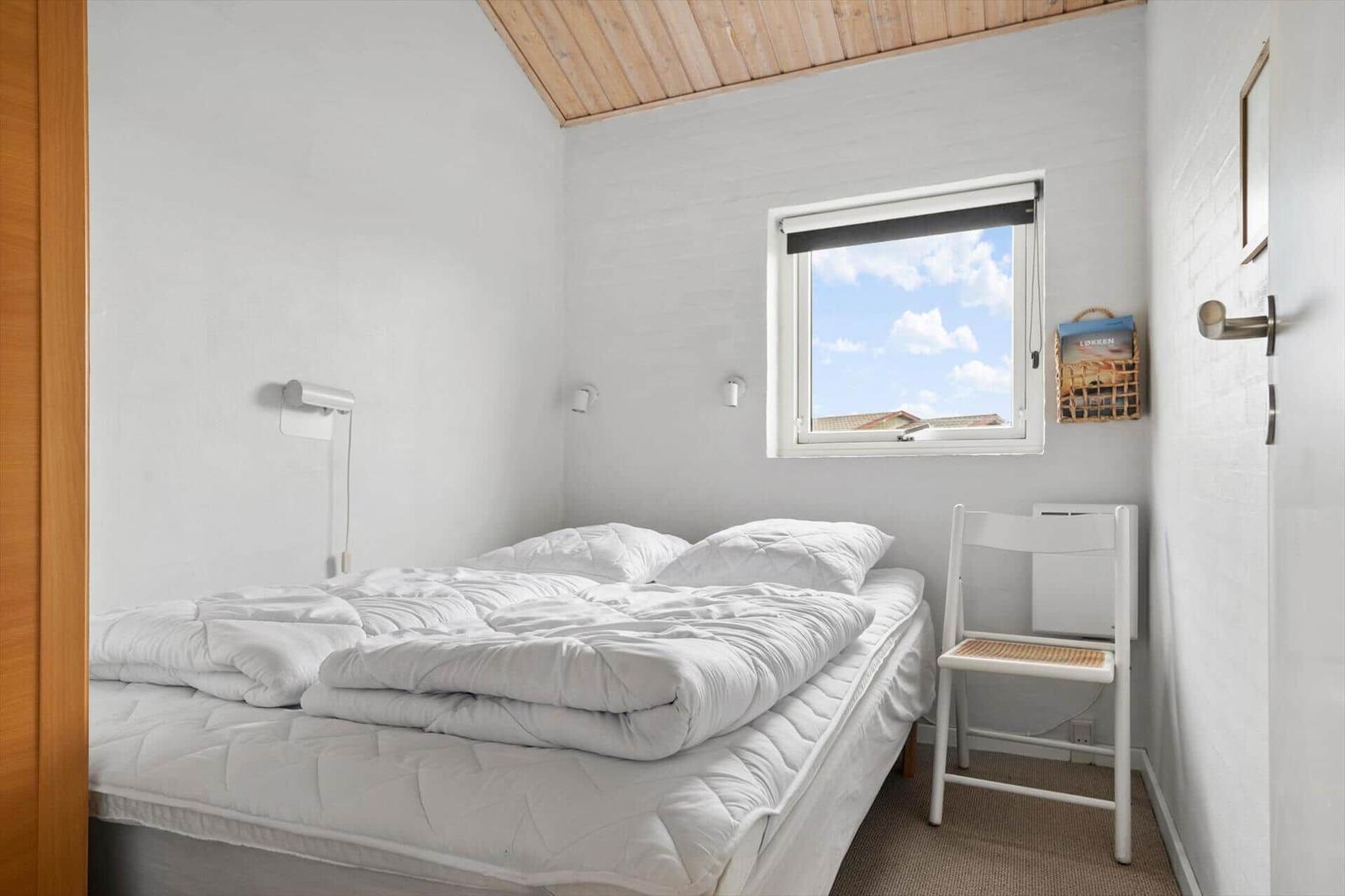 Bedroom with white bed, window and chair